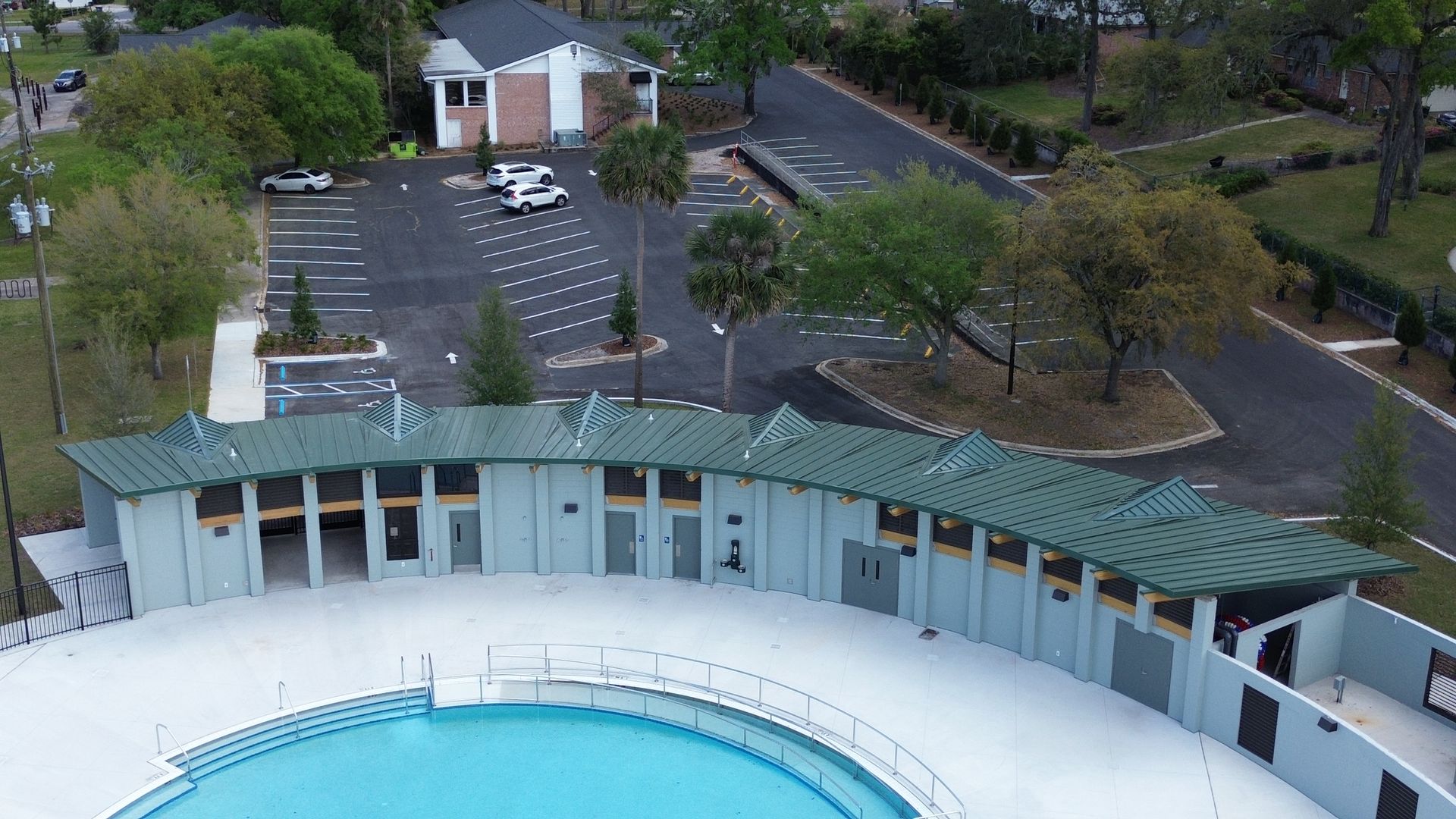 An aerial view of a public pool with a building and parking lot in the background.