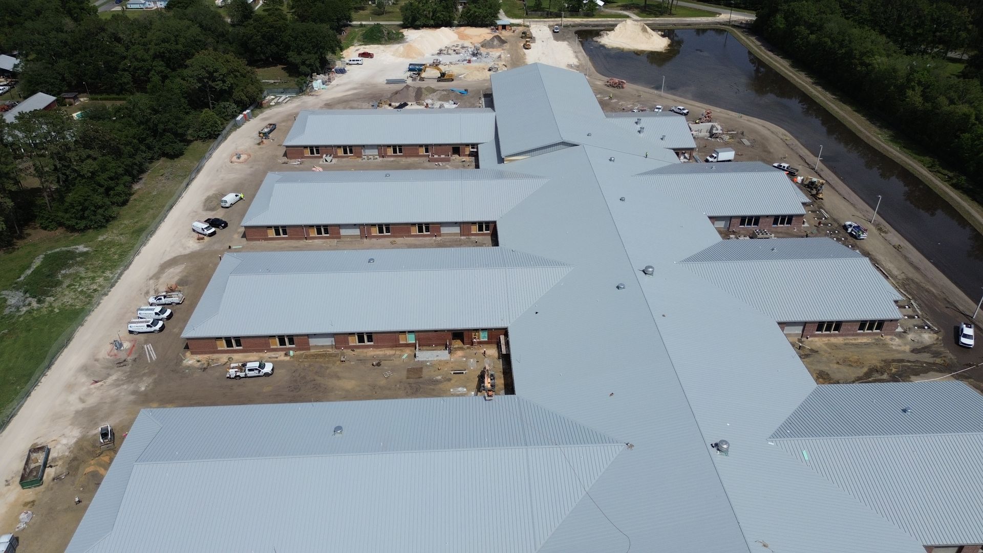 Overhead view of a building under construction with a gray metal roof. Construction equipment and materials are visible.