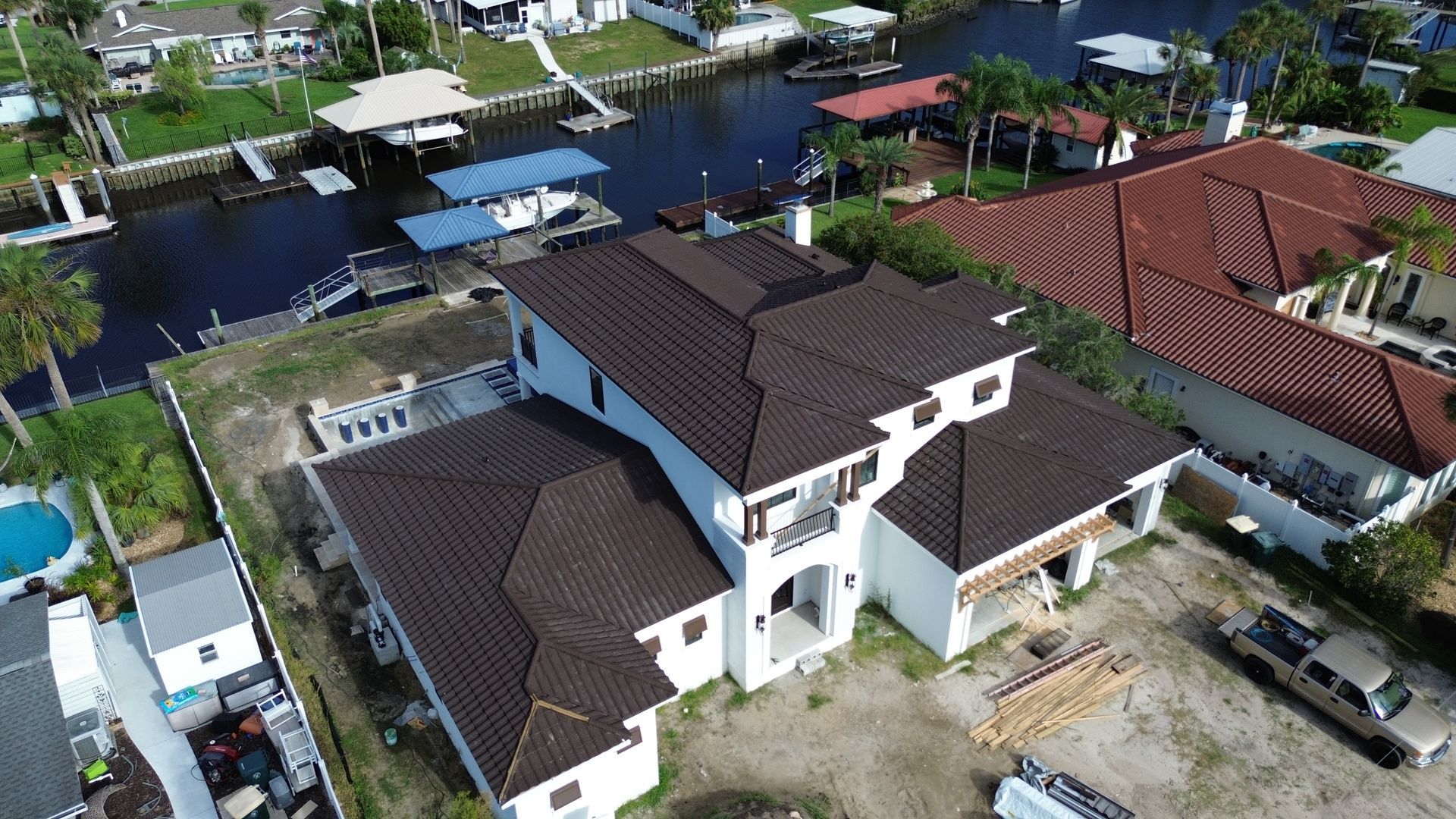 Aerial view of a white multi-story house with a brown tile roof near a waterway and other houses.