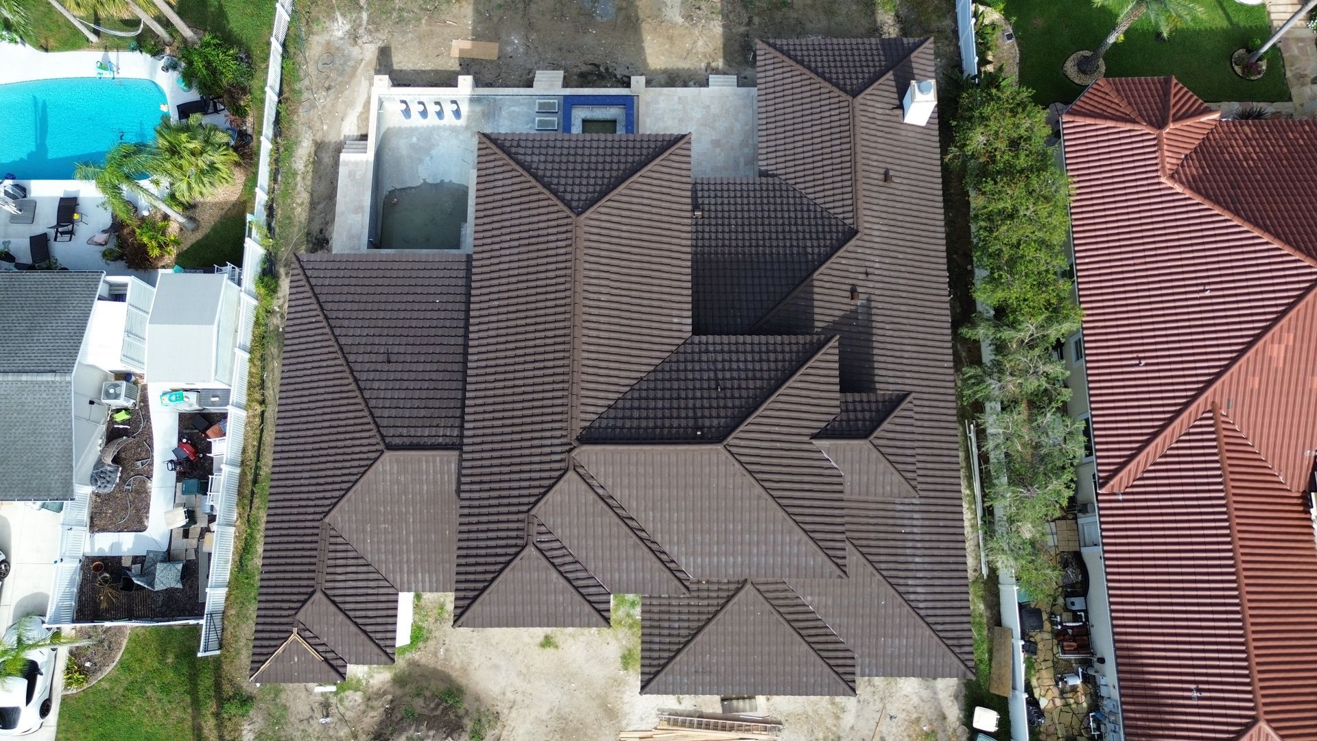 Overhead view of a house with a brown tile roof, pool, and surrounding foliage.