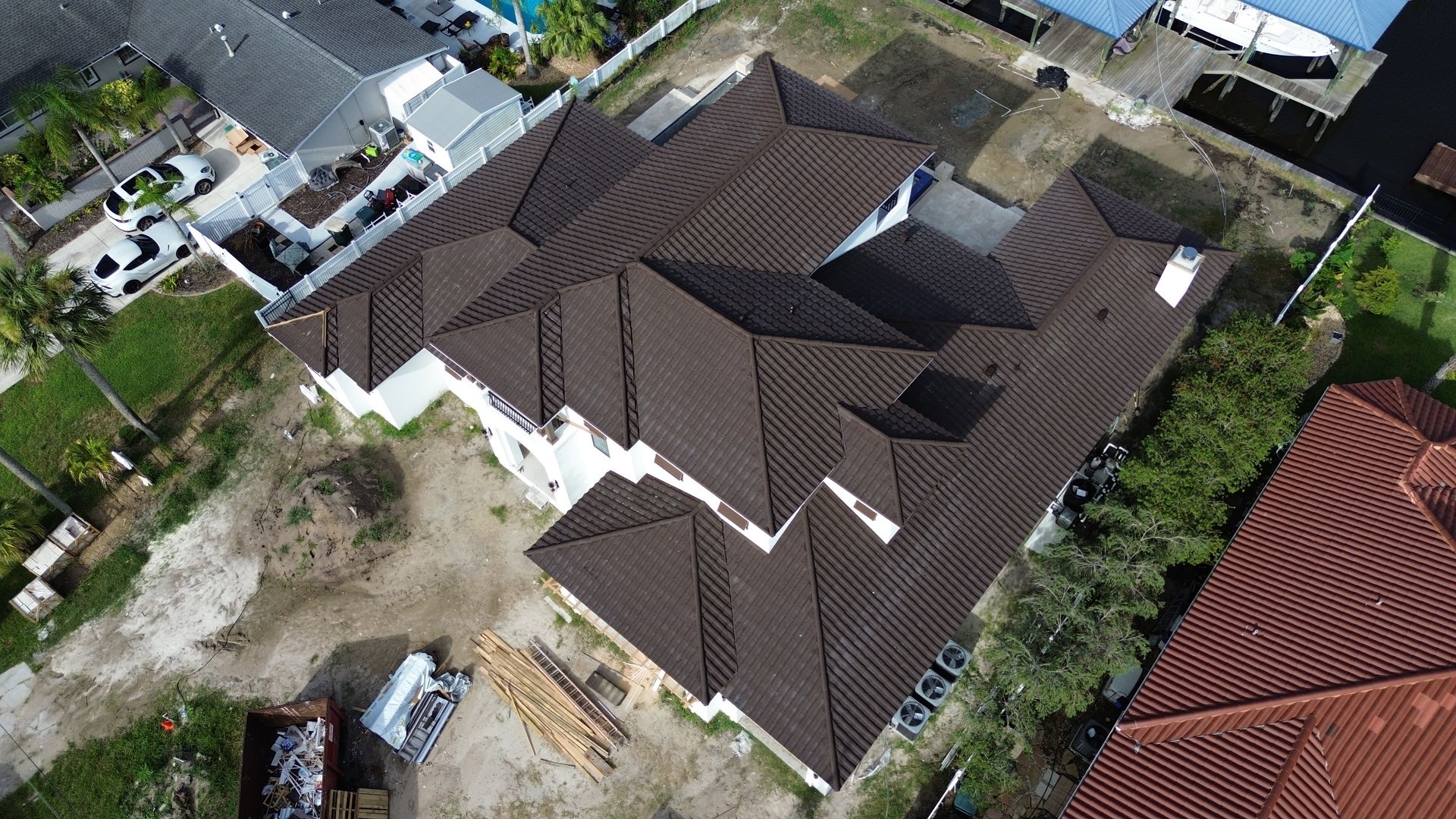 Overhead view of a house with a complex brown tile roof, surrounded by green grass and adjacent buildings.