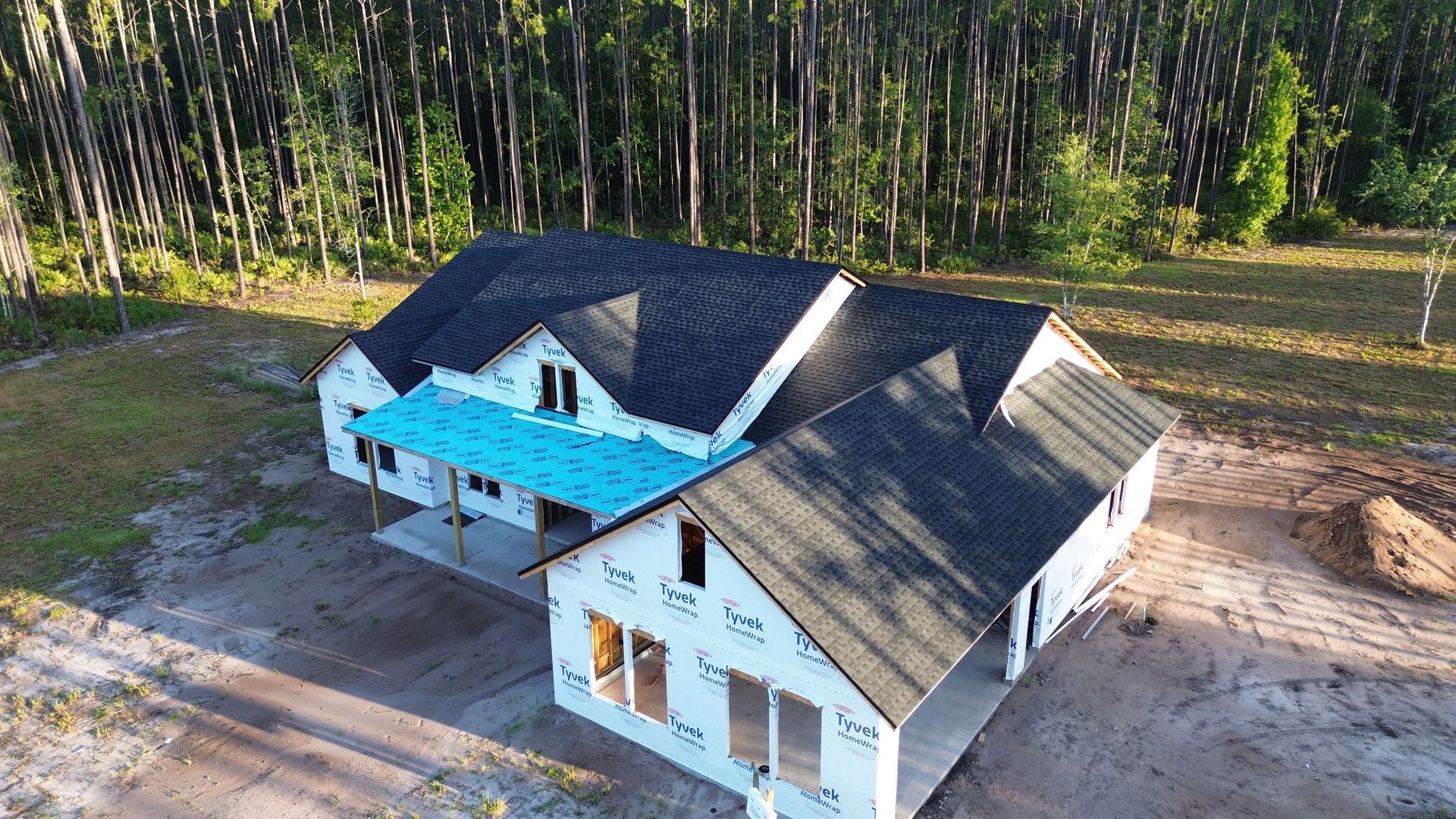 New house under construction with dark roof, surrounded by trees.