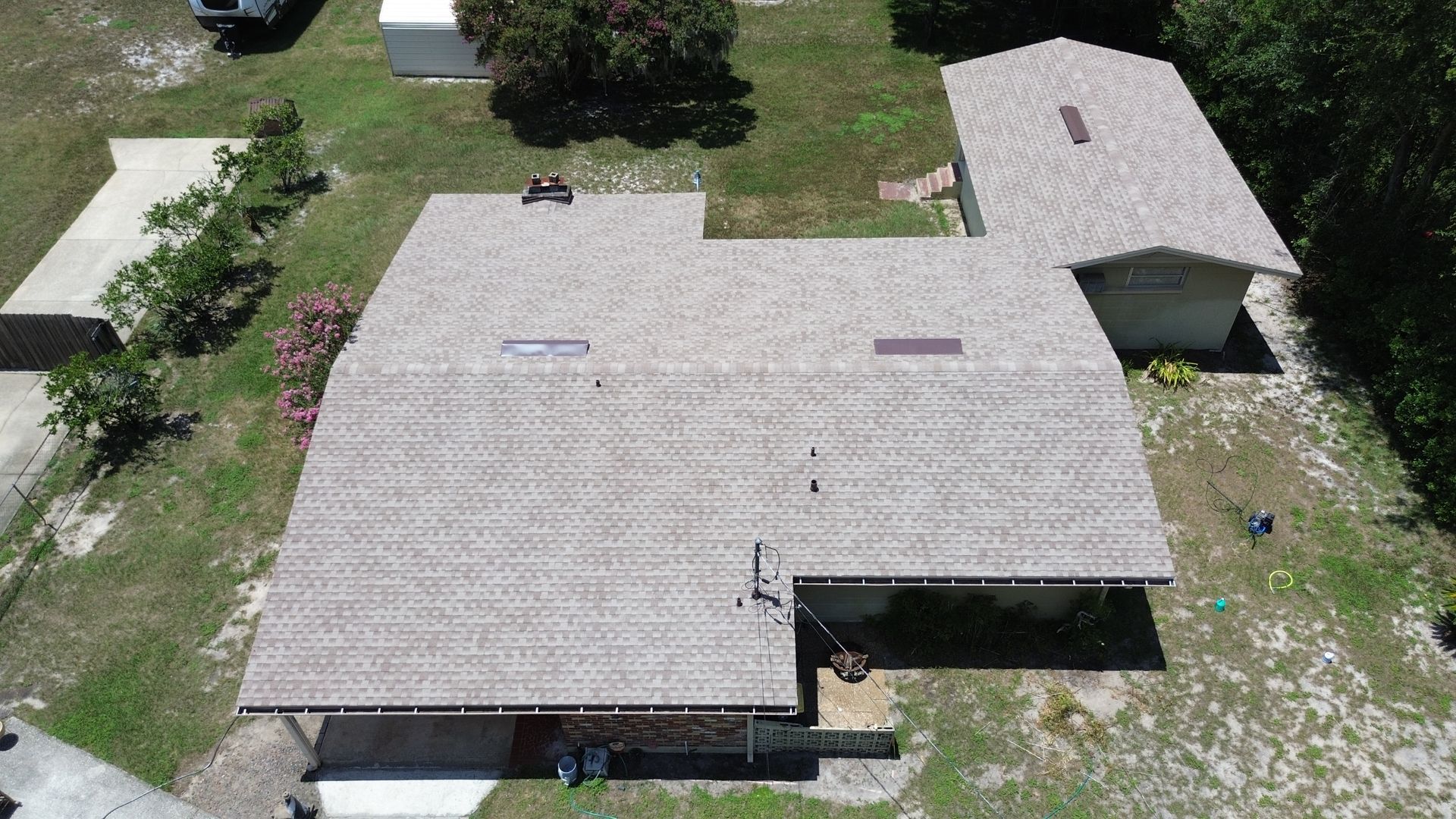Aerial view of a house with a light brown roof and a detached garage in a grassy setting.