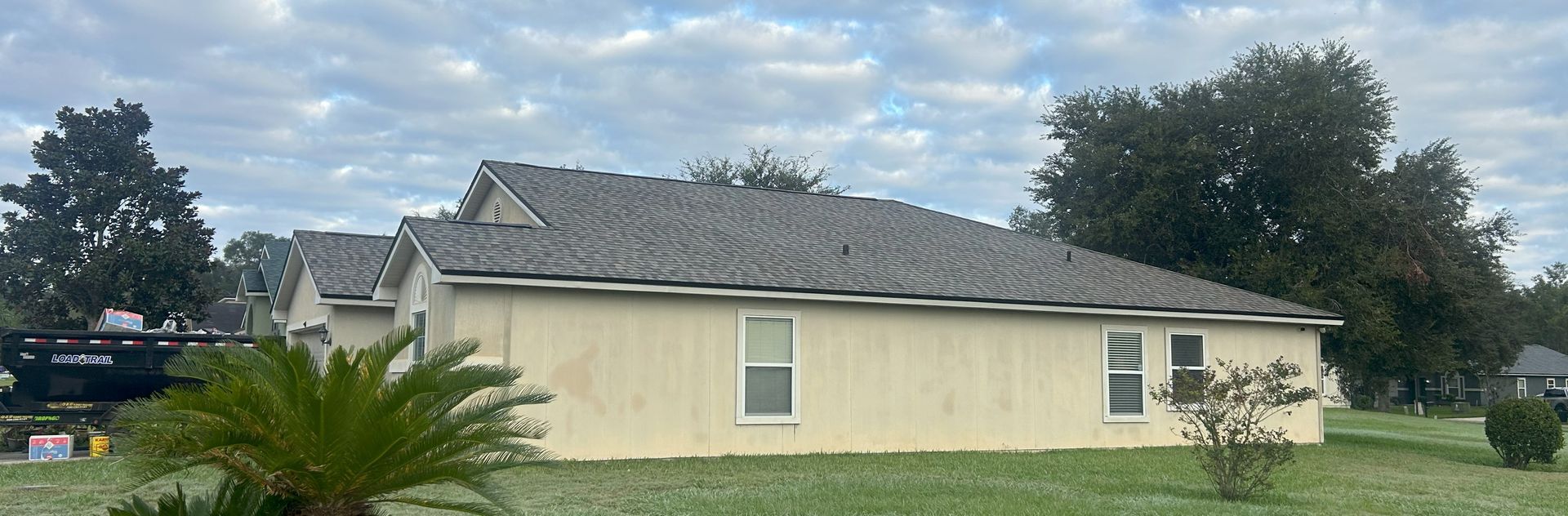 Beige house with gray roof, green grass, and cloudy sky.