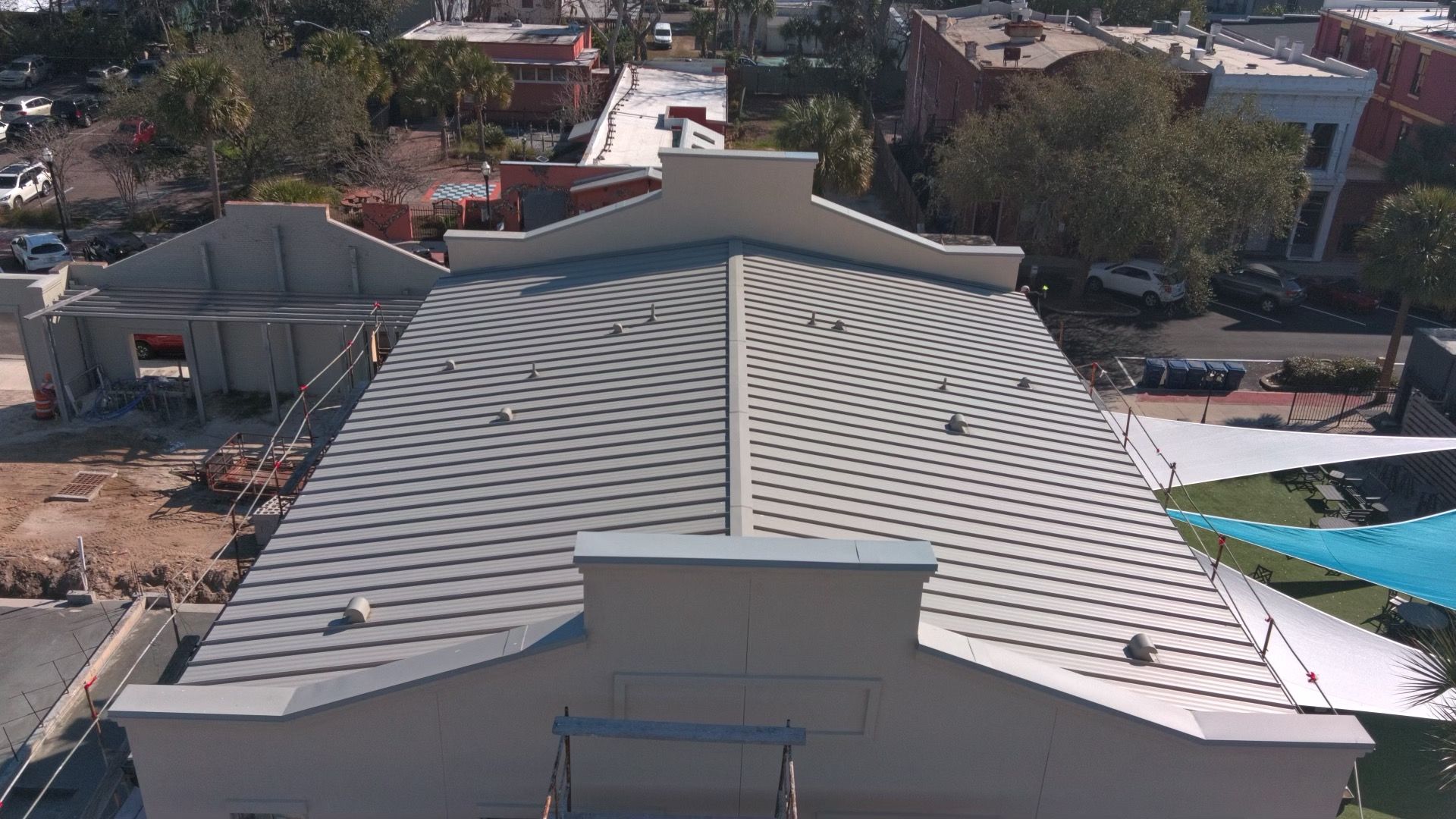 Overhead view of a building with a gray, textured roof; other buildings and trees are in the background.