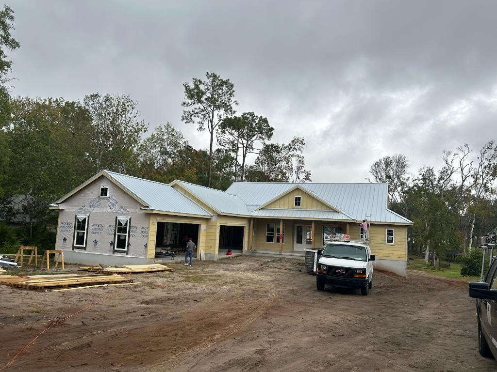 New house under construction with a metal roof and work truck. Cloudy sky.