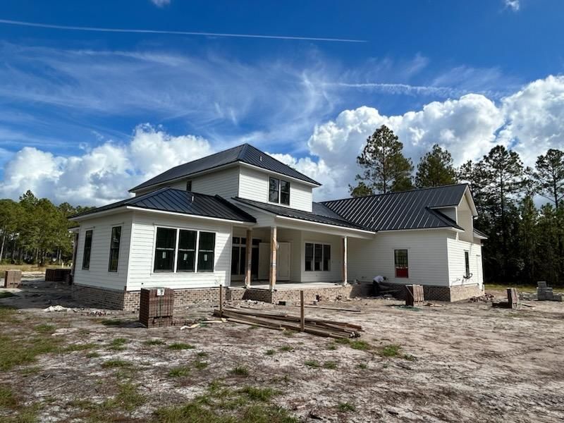 Two-story white house under construction with a black roof and blue sky.