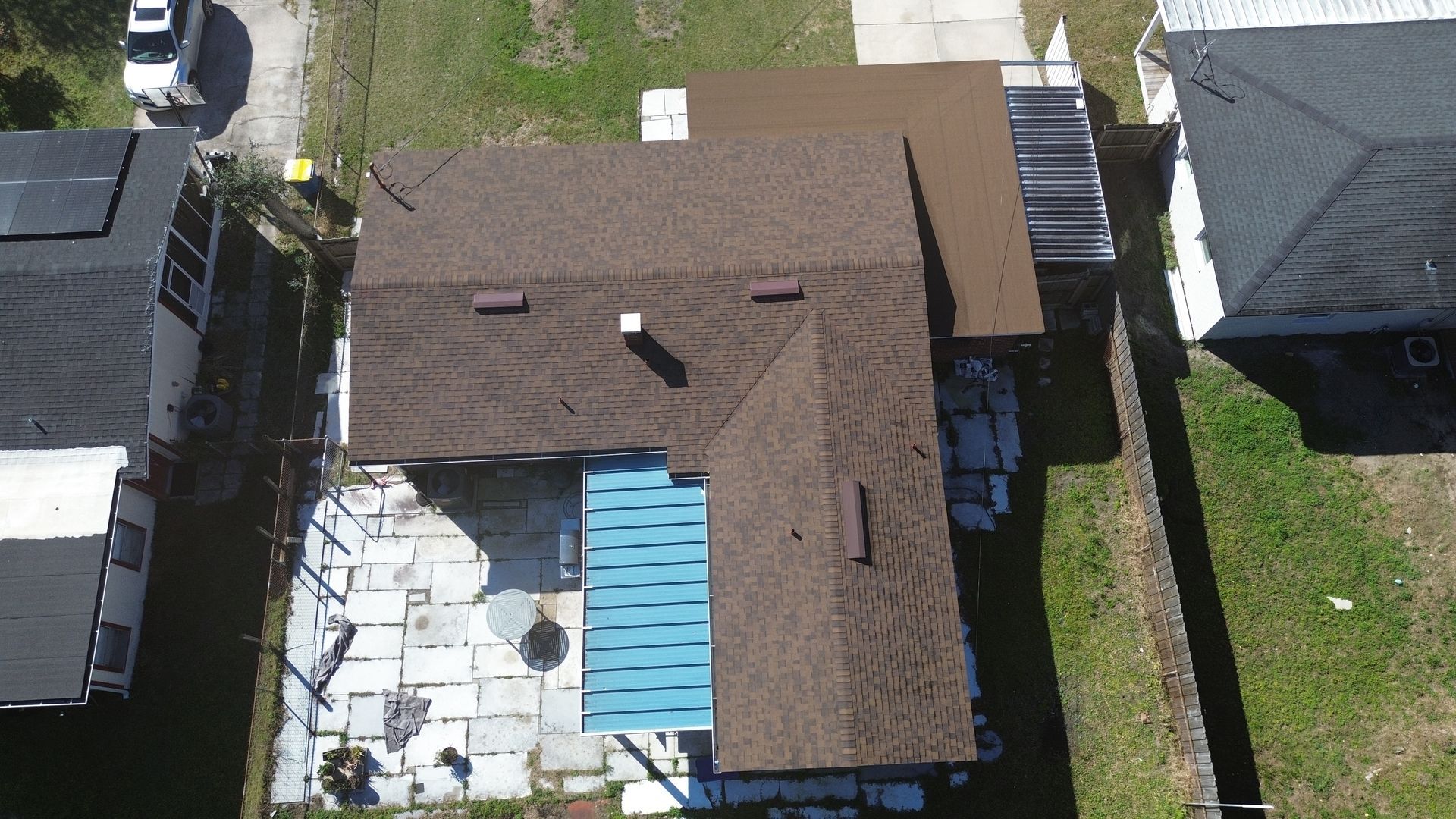 Overhead view of a house with a brown roof and blue patio area; adjacent to a lawn and neighboring houses.