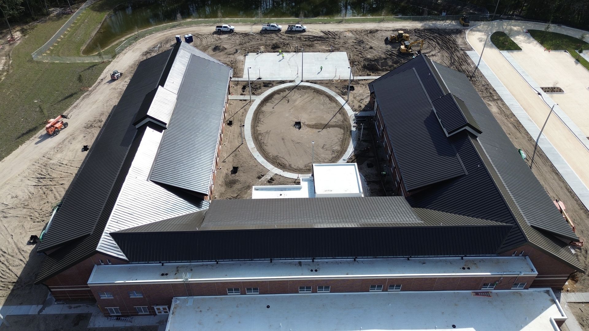 Aerial view of a building complex with dark roofs, a central circle, and construction equipment.
