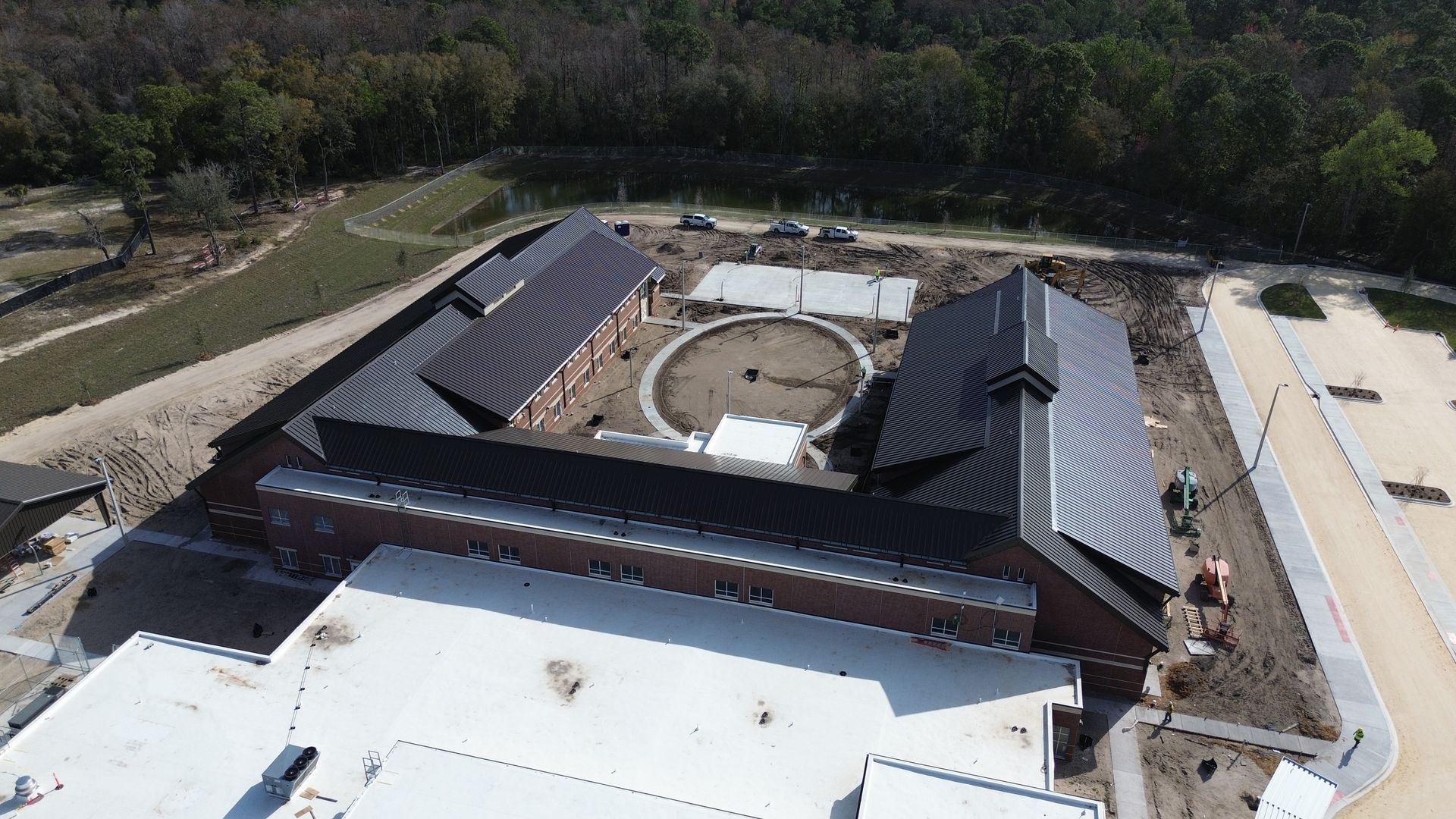 Aerial view of a complex with red brick buildings, dark roofs, and a circular courtyard, surrounded by landscaping.