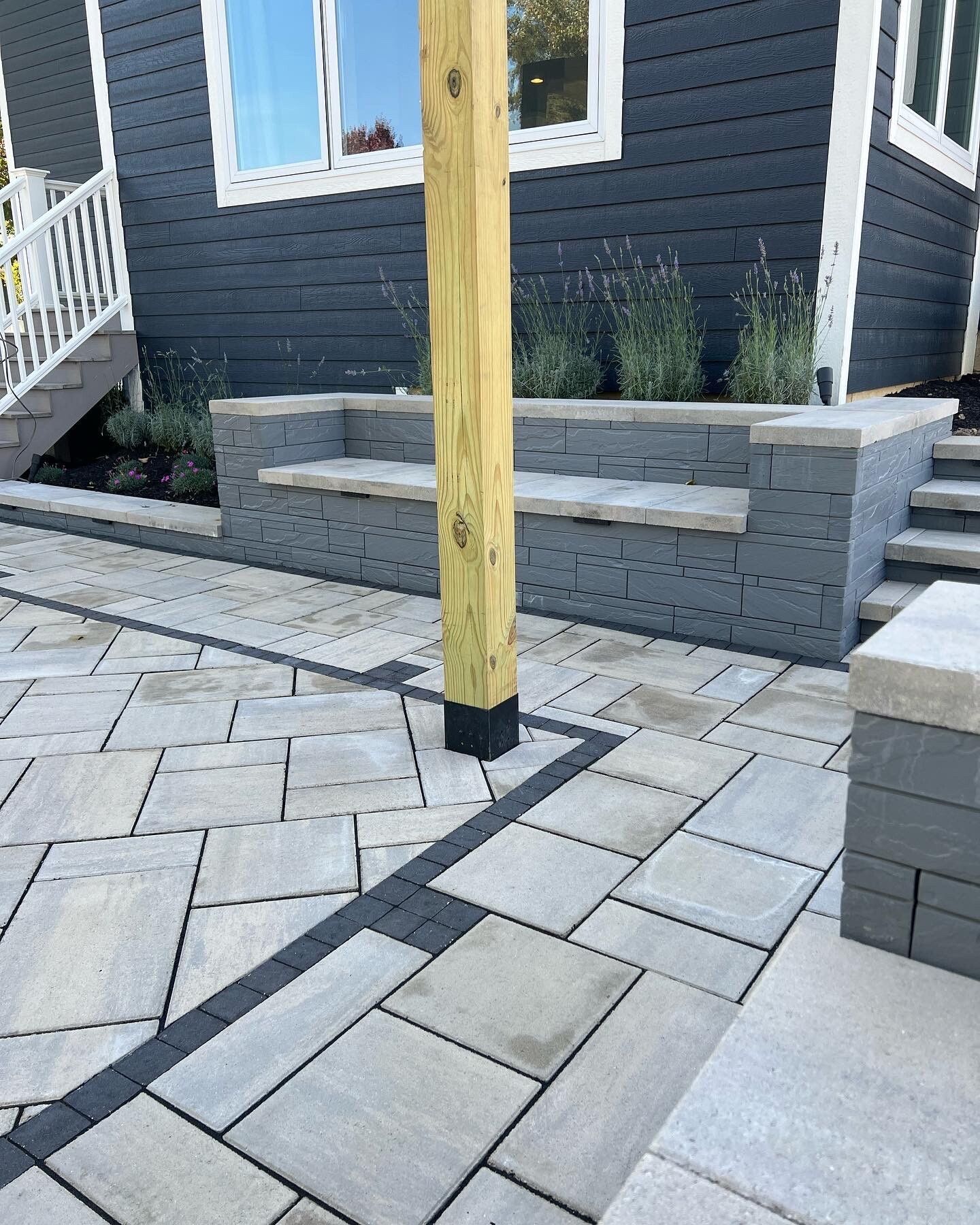 Stone patio with gray walls and stairs. Wooden pole in center. Blue-gray house.