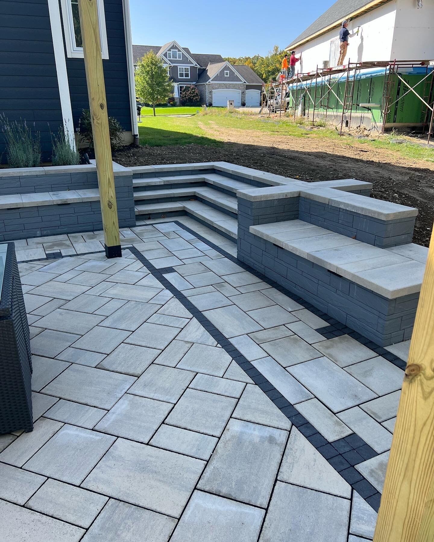 Patio with light gray pavers, dark border, built-in benches, and steps. Wooden posts support a structure.