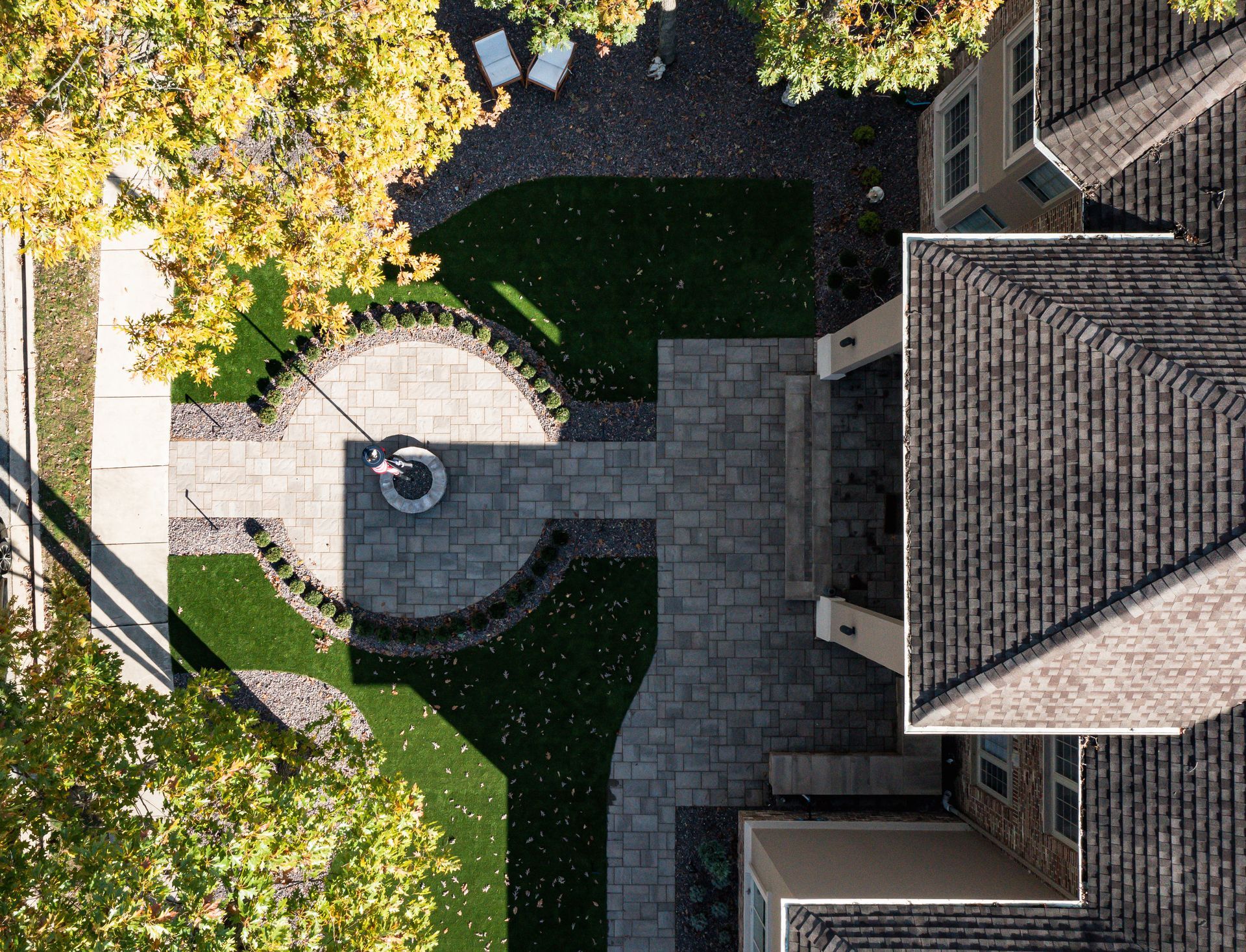 Overhead view of a house with a stone patio, green lawn, and brown roof. Trees with yellow leaves.