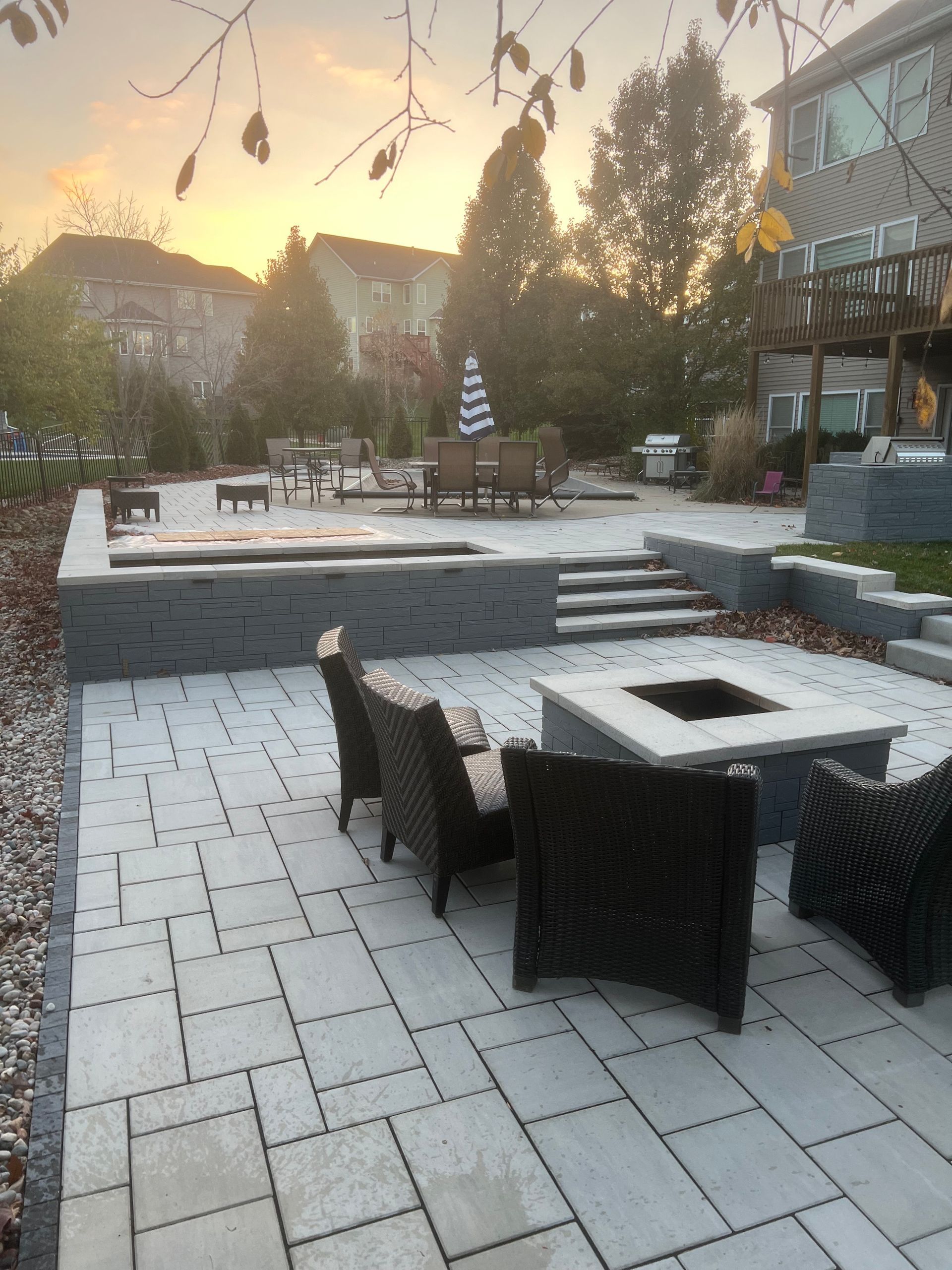 Patio with stone pavers, chairs, fire pit, hot tub, and steps, at sunset.