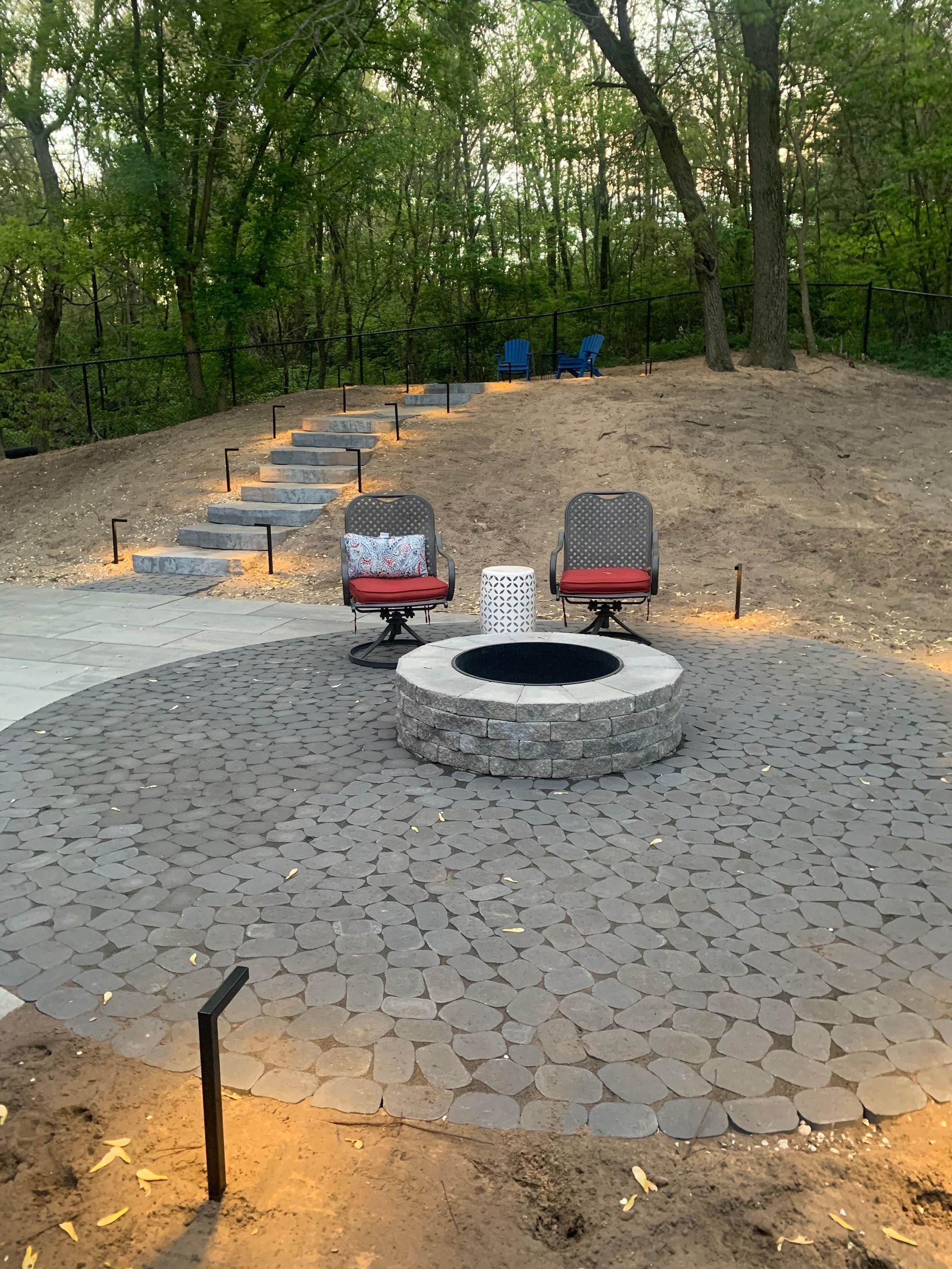 Fire pit area with two chairs, stone patio, steps leading up a hill.