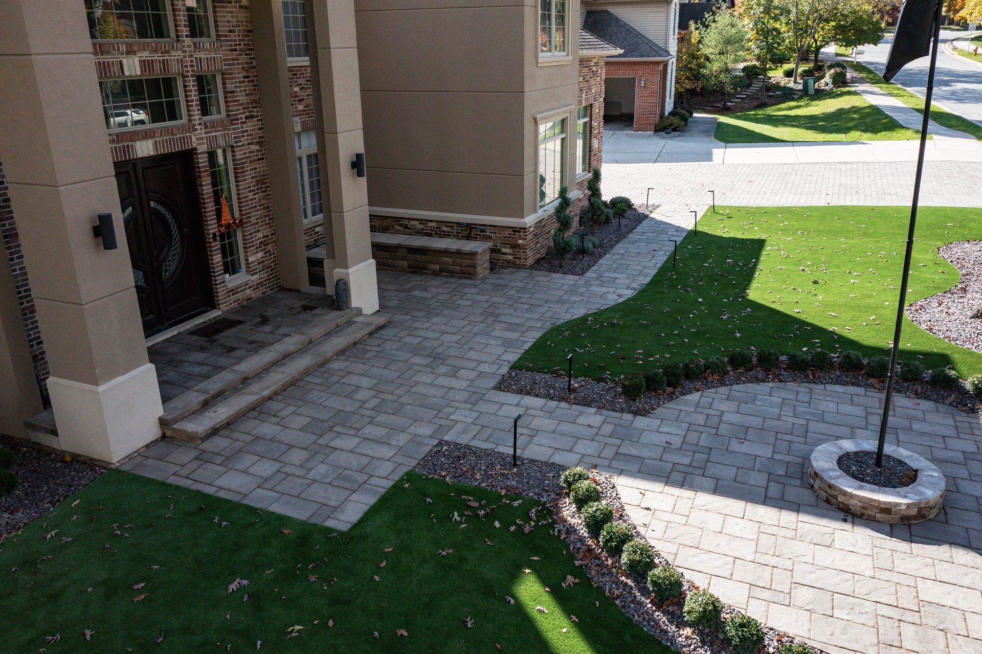 A house exterior with paved entrance, green lawn, landscaping, and a fire pit.