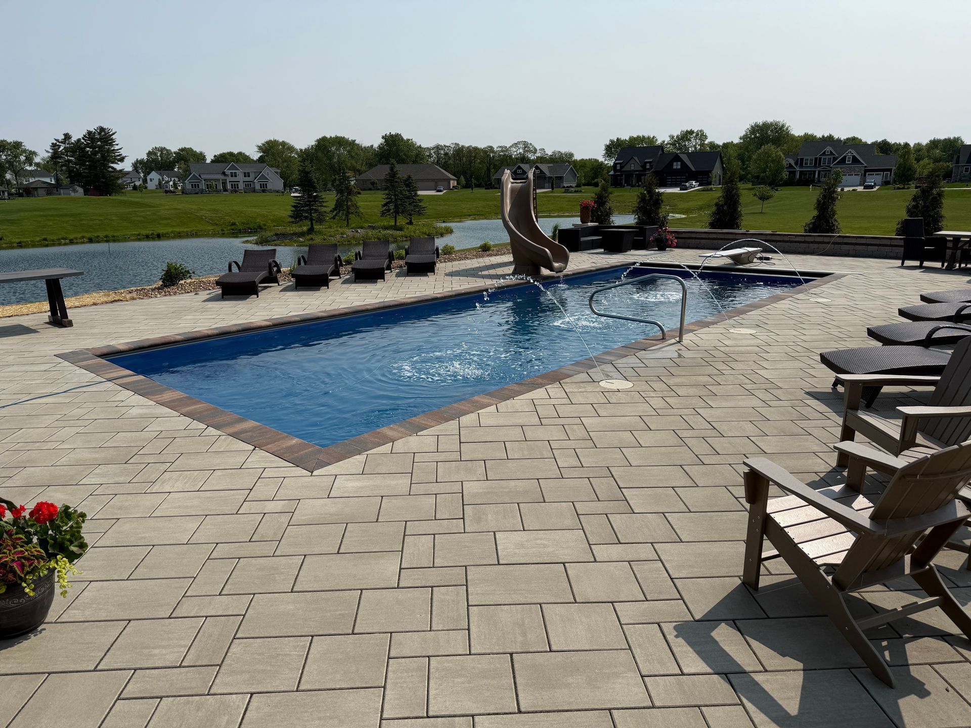 Aerial view of a backyard with a fire pit, hot tub, putting greens, and a multi-level deck on a house.