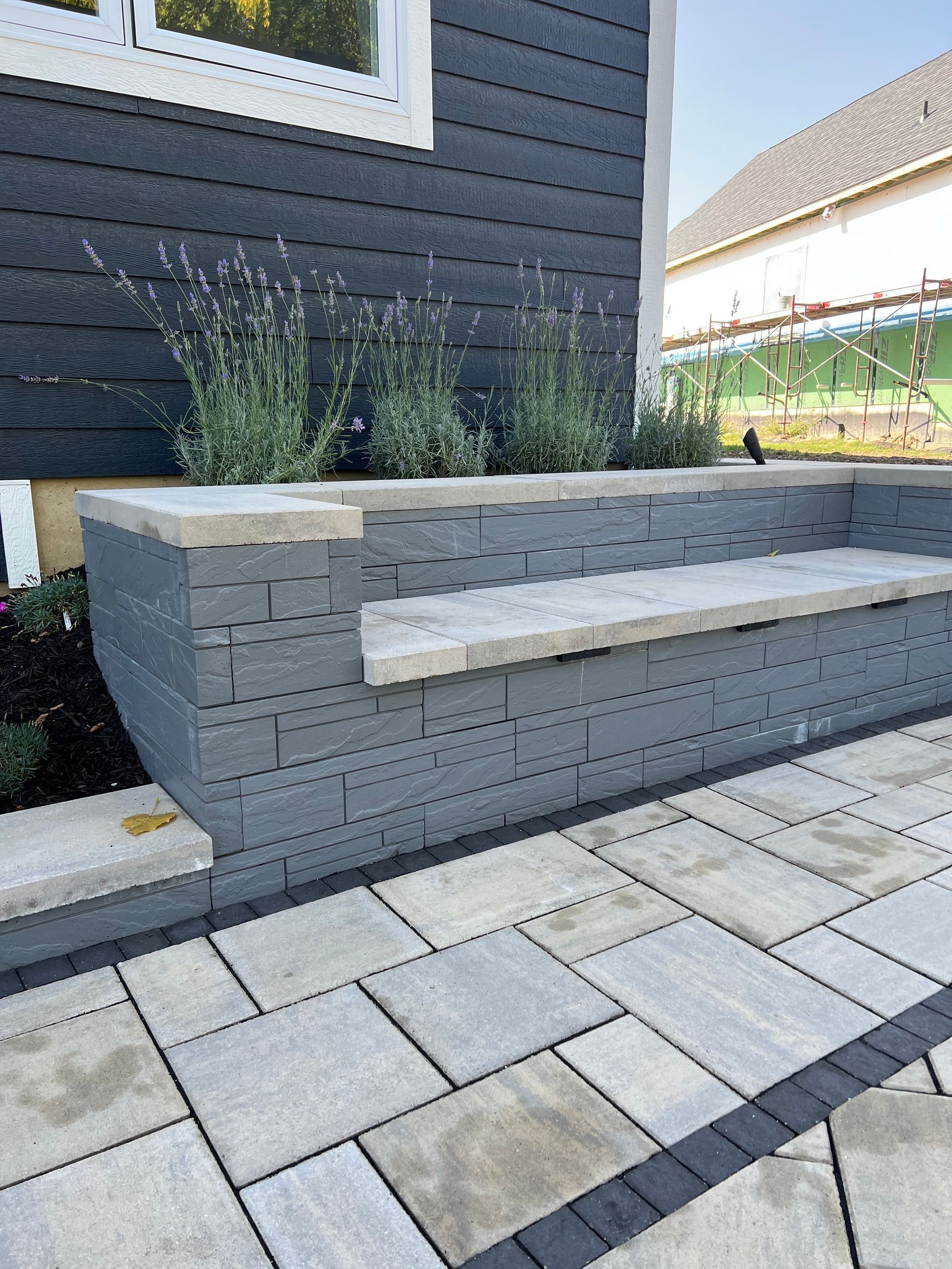Grey stone patio with built-in bench, lavender plants, and dark blue siding.