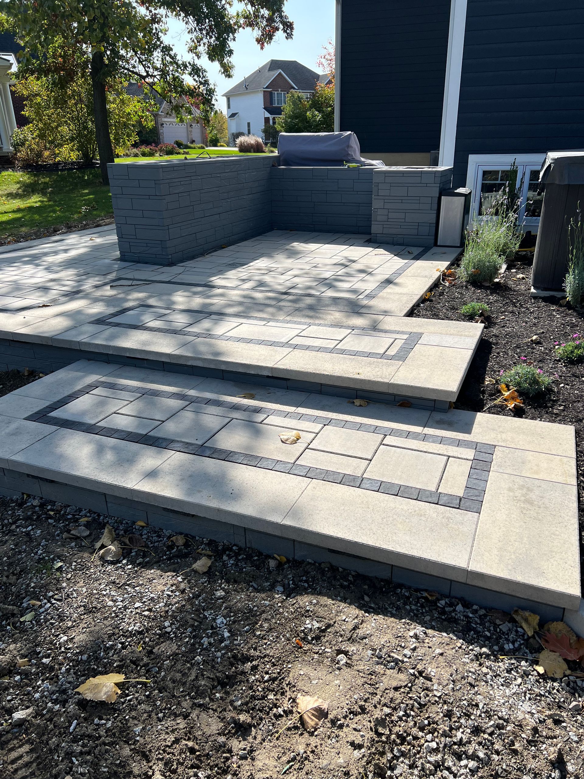 Paver patio with steps and retaining wall. Gray and tan pavers with a dark border.
