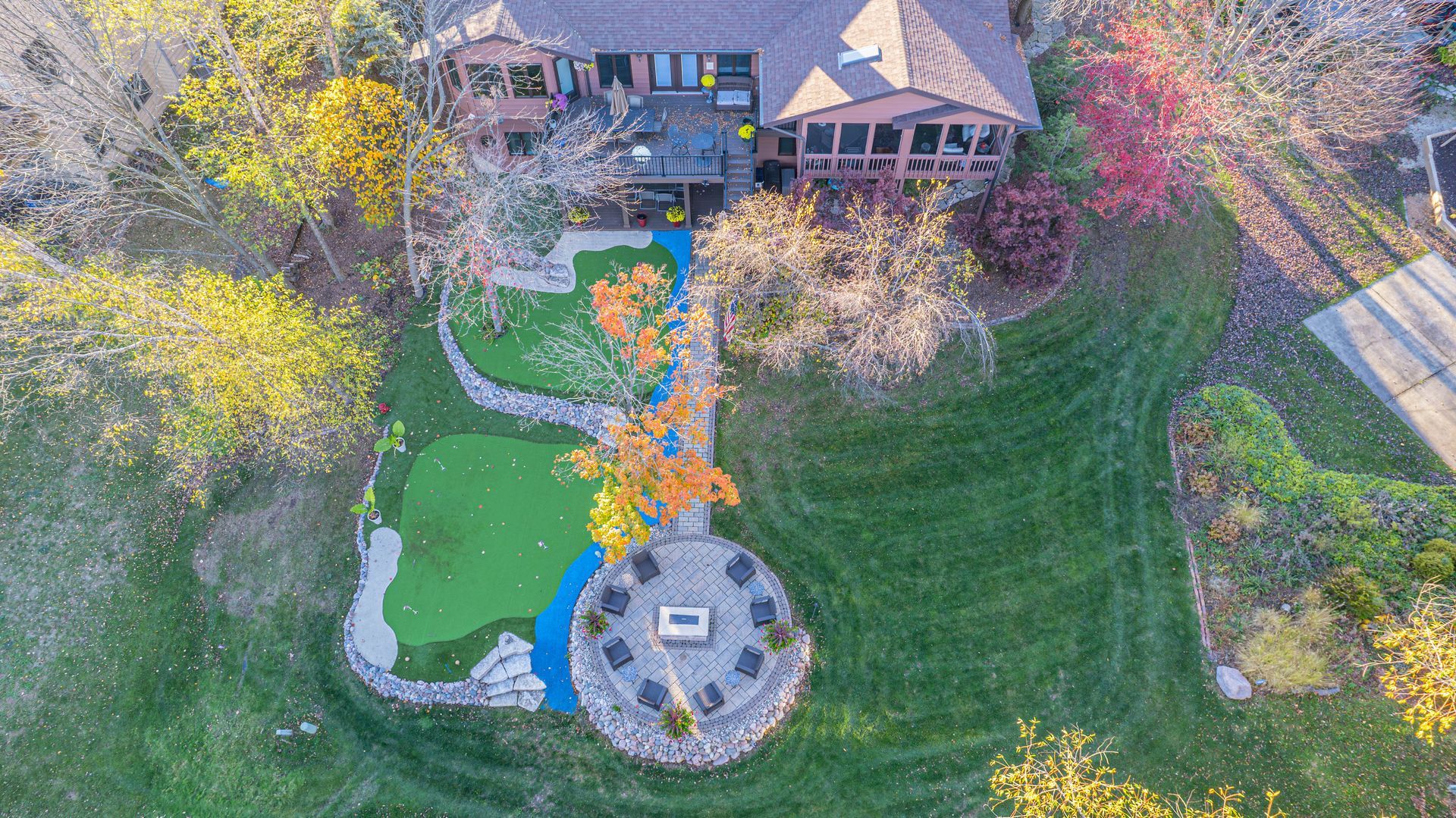 Overhead view of a house with a green lawn, putting green, fire pit, and autumn trees.