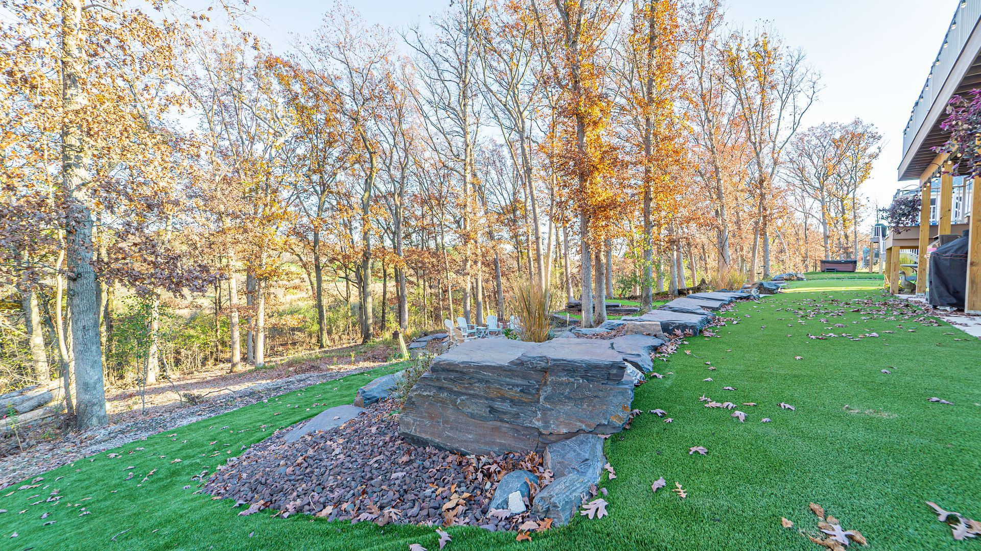 Lush green lawn with large rocks and trees, autumn leaves, next to a building.