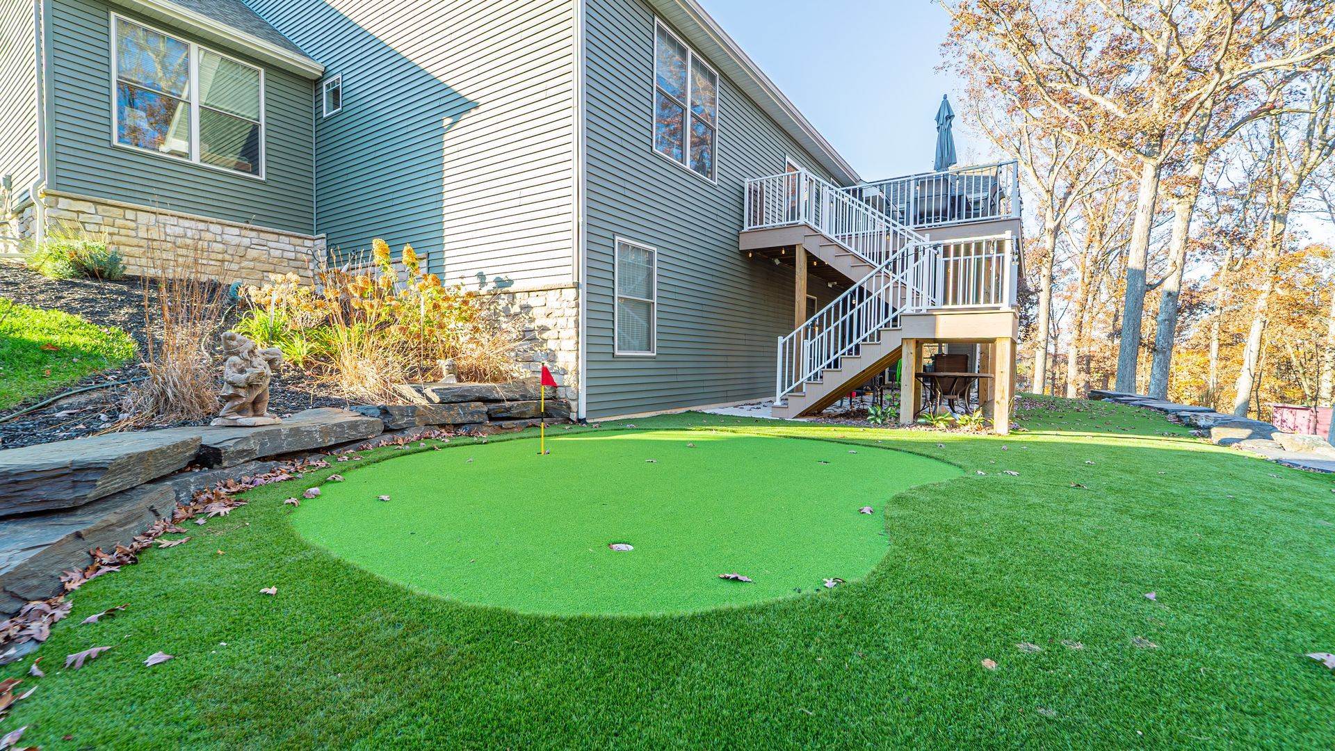 Green putting green in backyard of a two-story home with wooden deck stairs.
