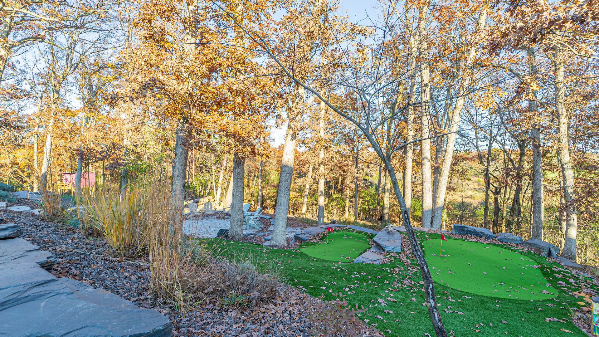 A backyard putting green surrounded by trees with fall foliage.