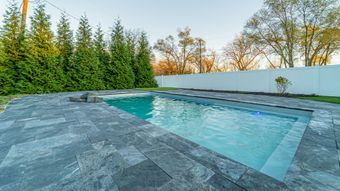 Elegant white house with gray brickwork and paved driveway. Landscaping includes stone walls, plants, and lamp posts.