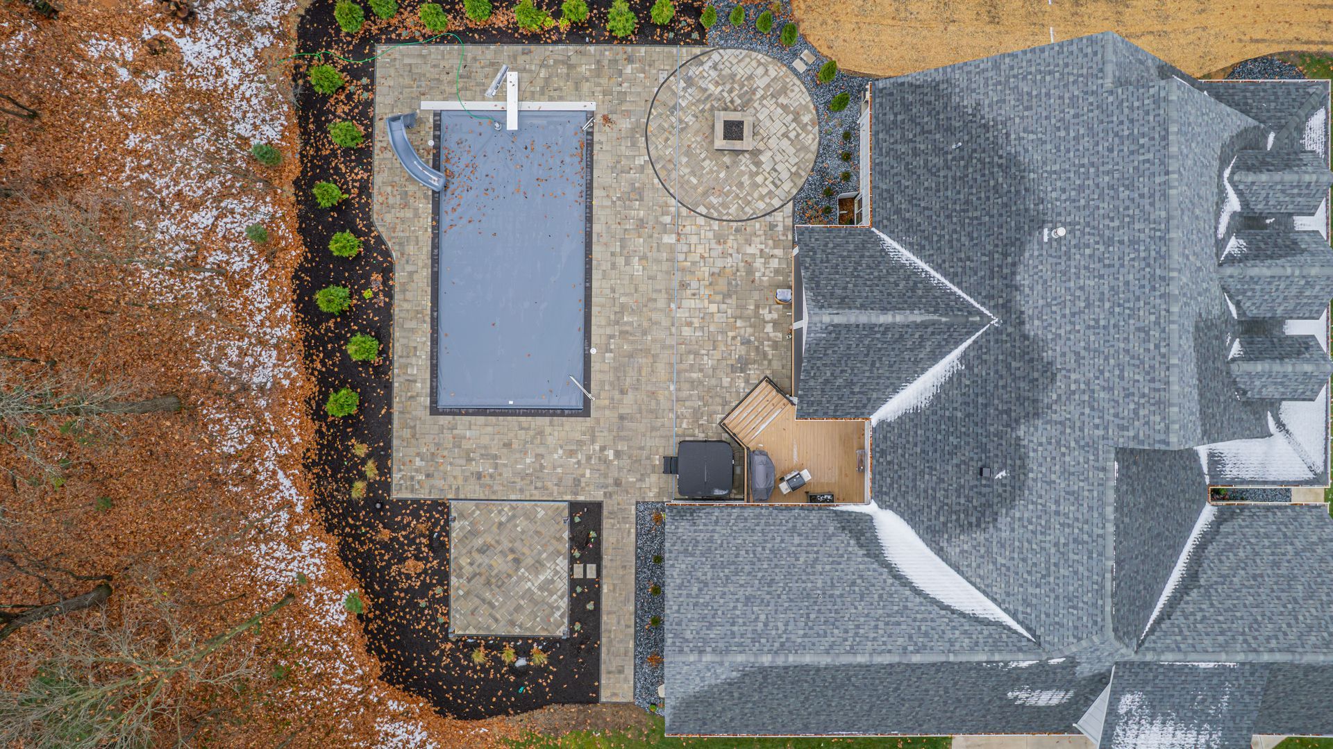 Overhead view of a house with a pool, patio, and partially snow-covered roof, surrounded by brown foliage.