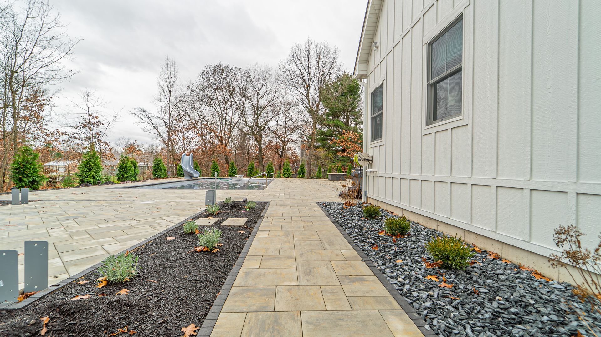 Path of paving stones leads to a stone patio next to a white house with a landscaped yard.