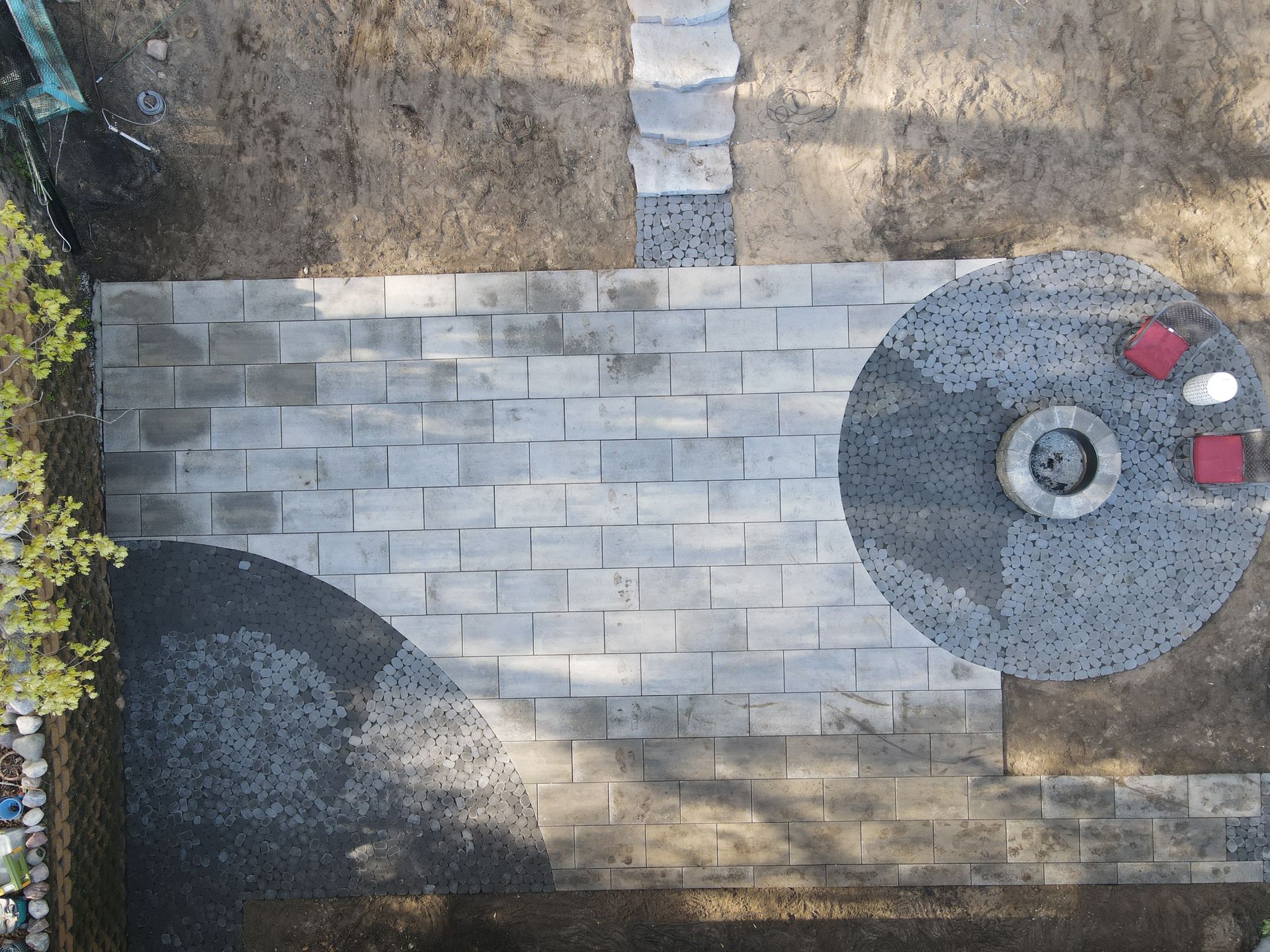 Overhead view of a backyard patio with a fire pit, seating, and stone pathways.