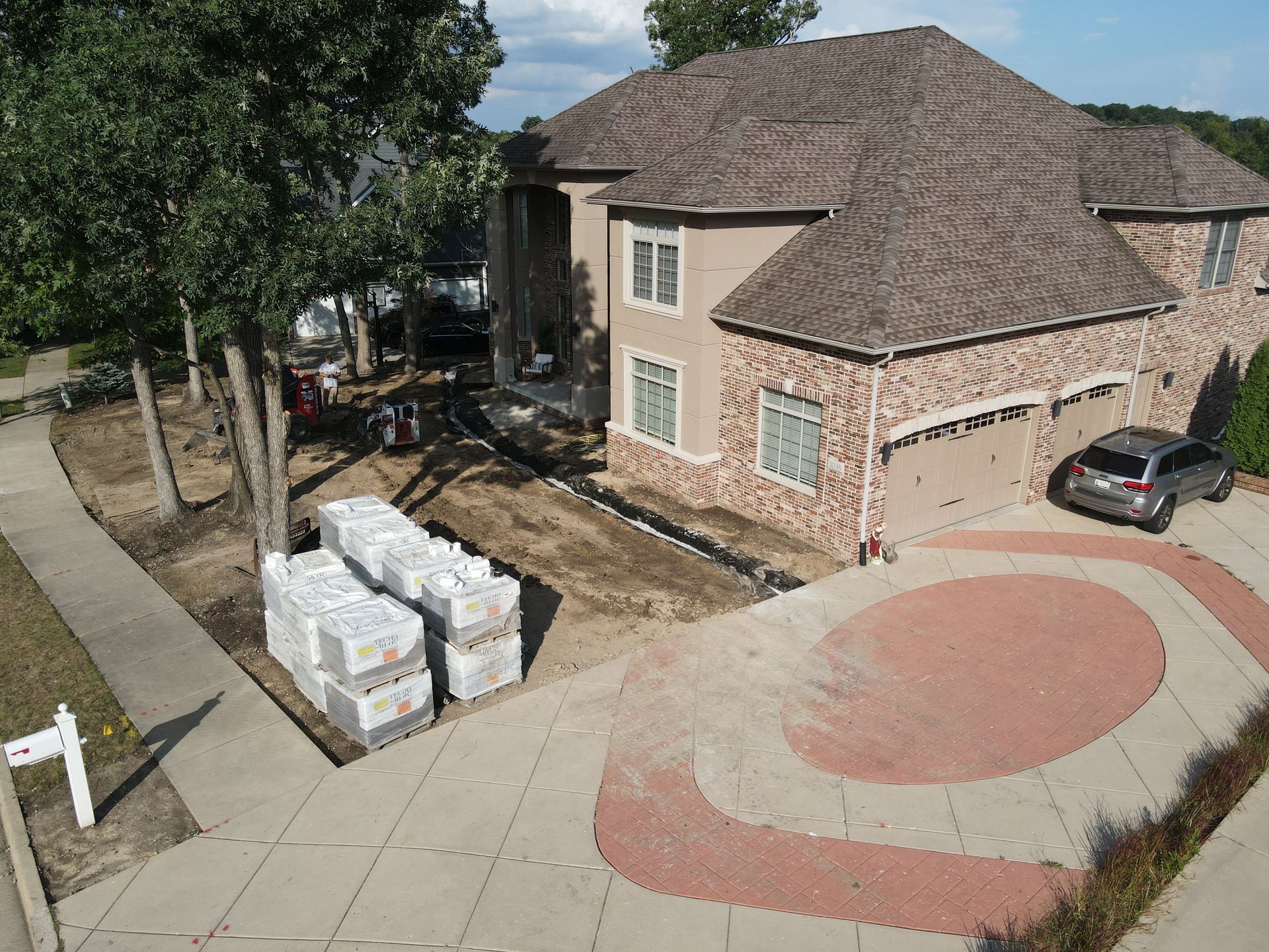 Brick house with brown roof, driveway with brick accents, and stacks of pavers on the side.