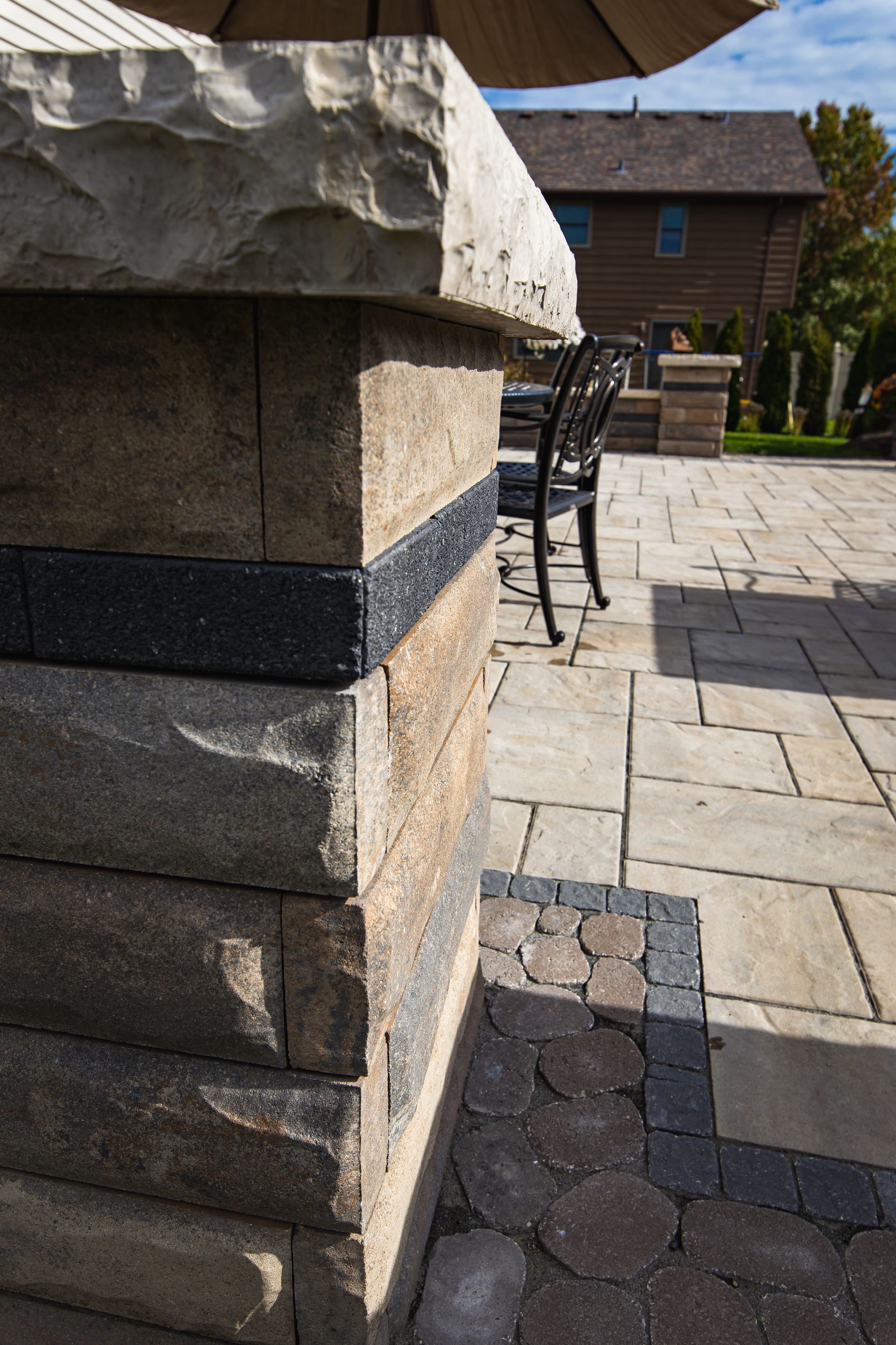 Stone pillar with black stripe detail, integrated into a patio with wooden building in the background.