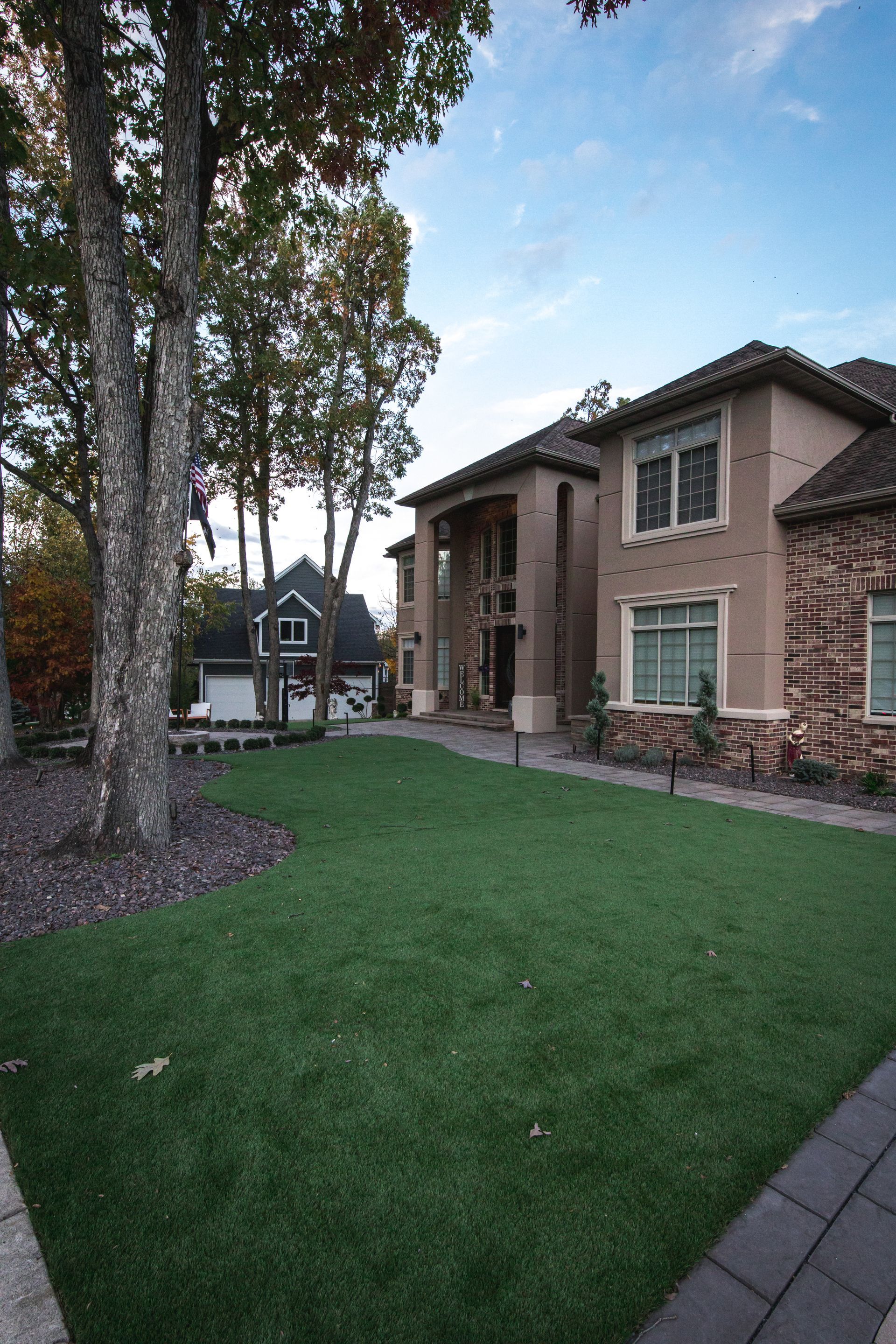 Large house with manicured green lawn and trees, blue sky in the background.
