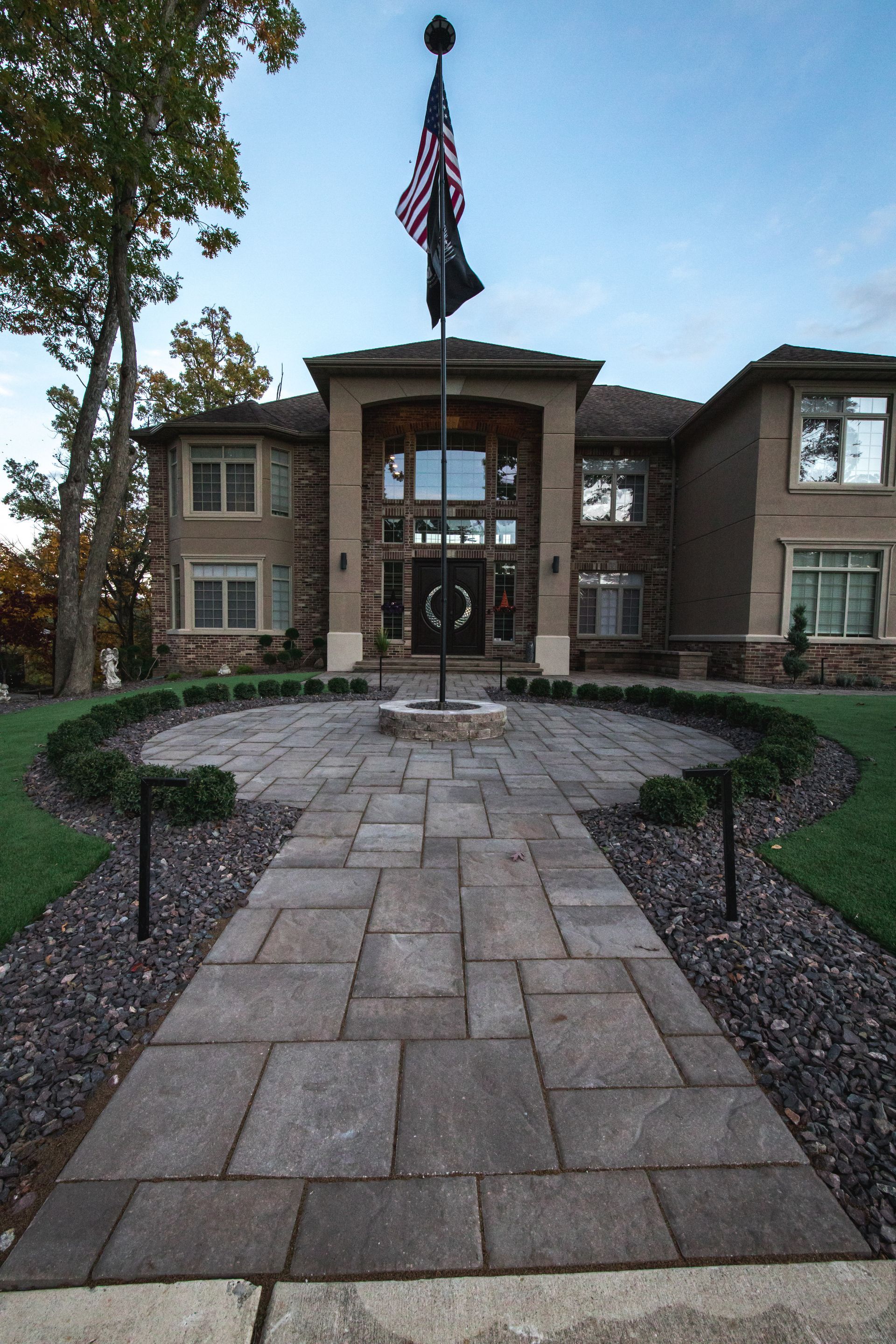 A large house with a stone pathway leading to the entrance, a flag pole with an American flag flies above the house.
