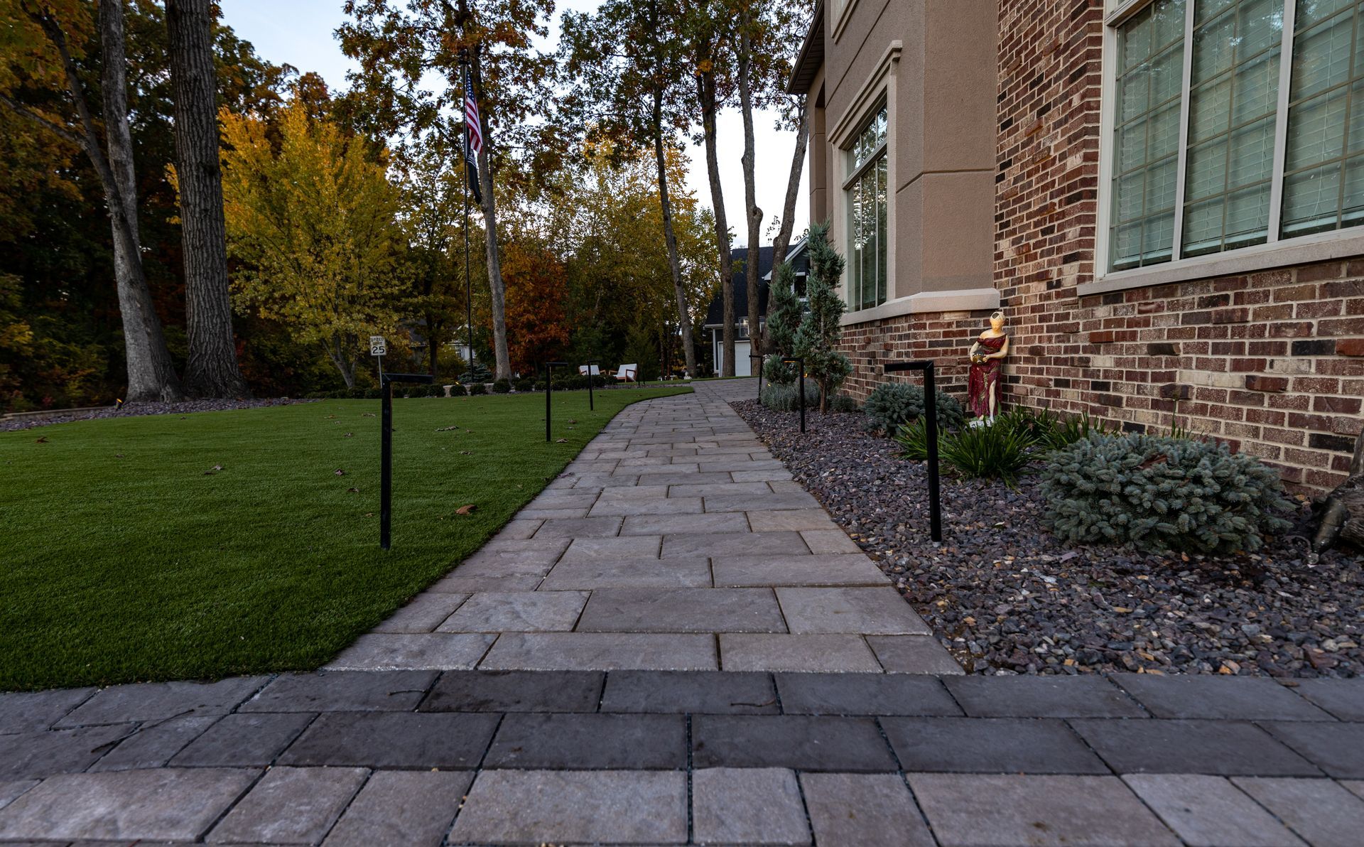 Brick walkway leading towards a building with landscaping and trees in autumn.