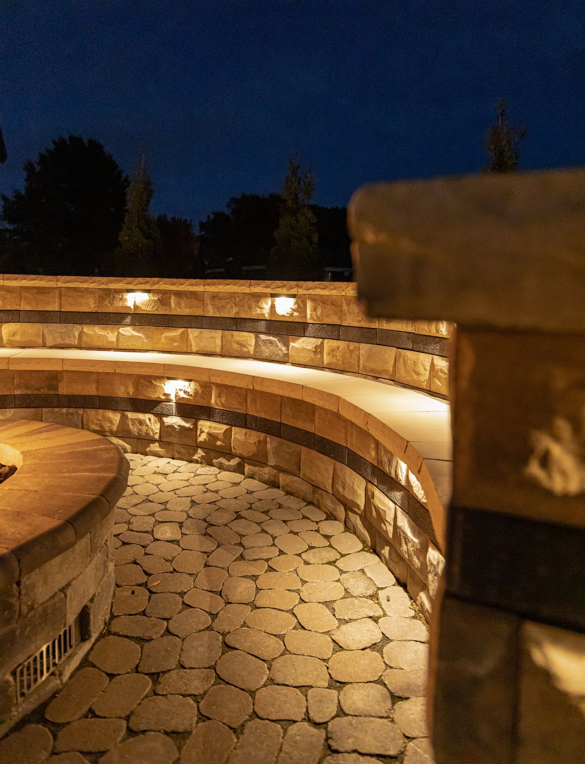 Stone patio with tiered seating, illuminated by warm lights at night.