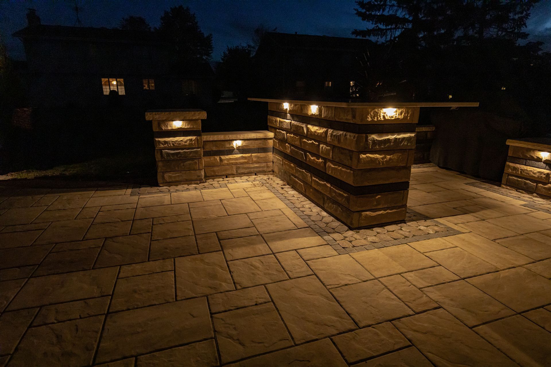 Outdoor patio at night with illuminated stone walls and paving stones.