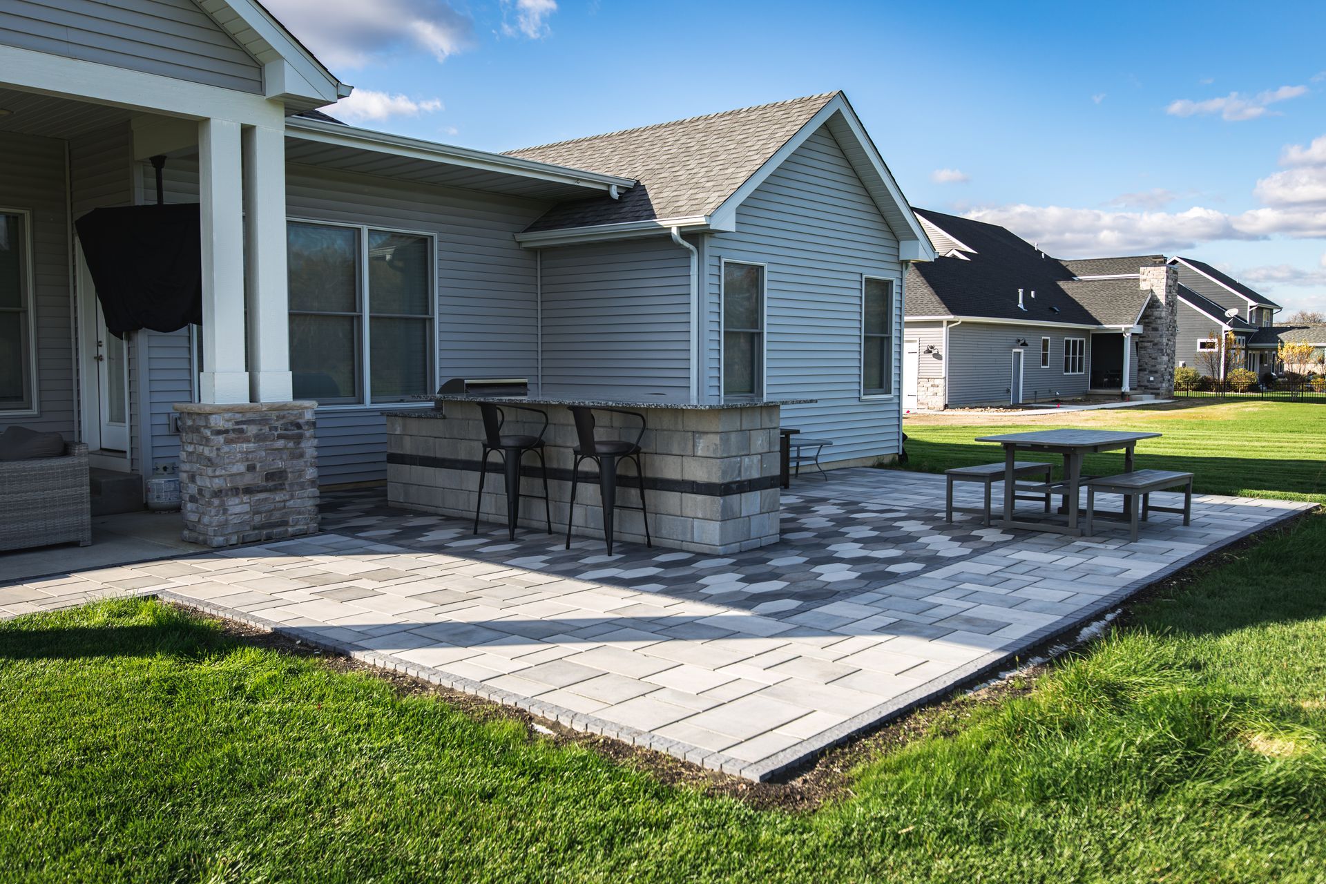 Patio with bar, picnic table, and house, on a sunny day.
