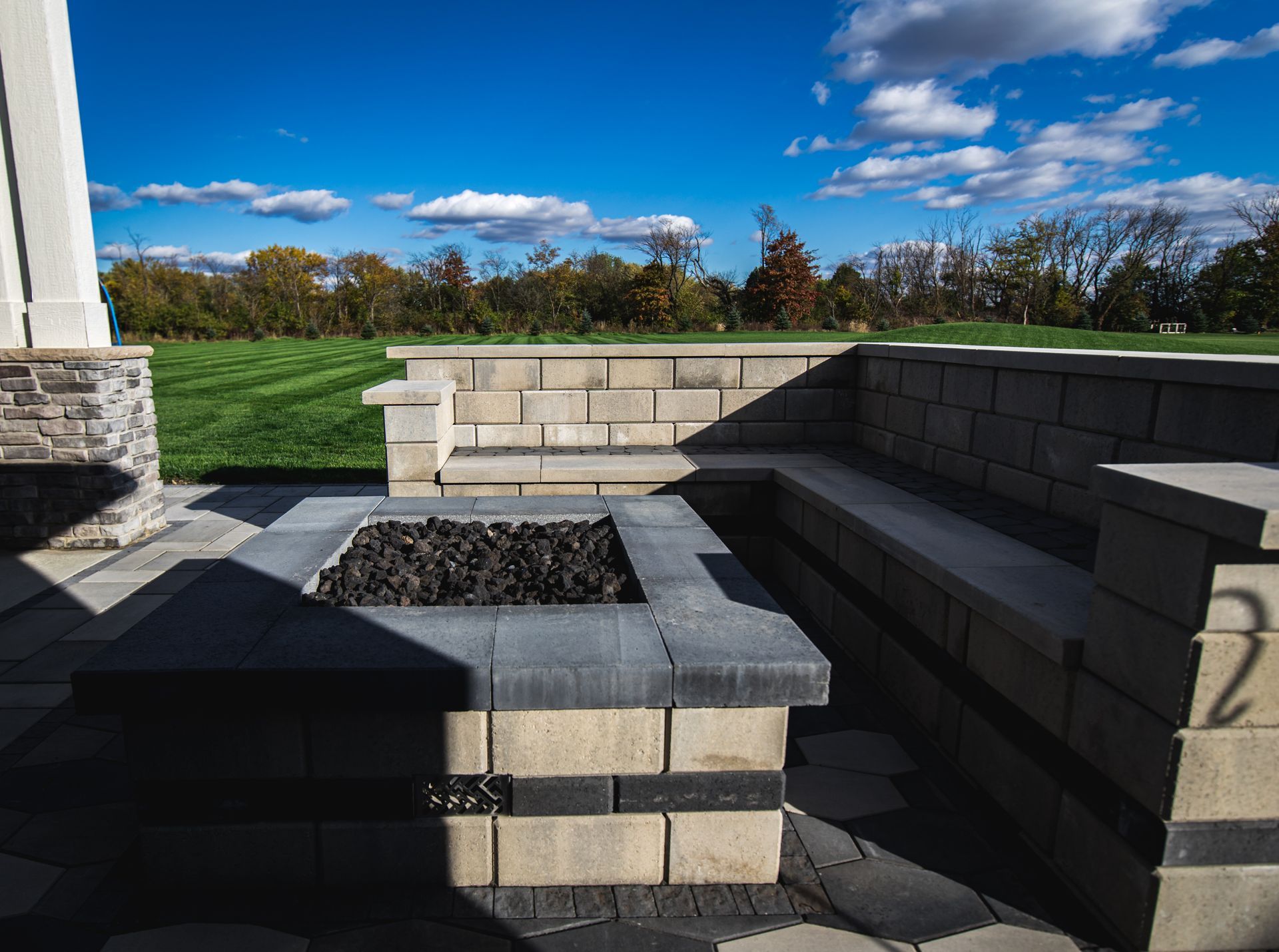 Stone fire pit with built-in seating on a patio, sunny day.