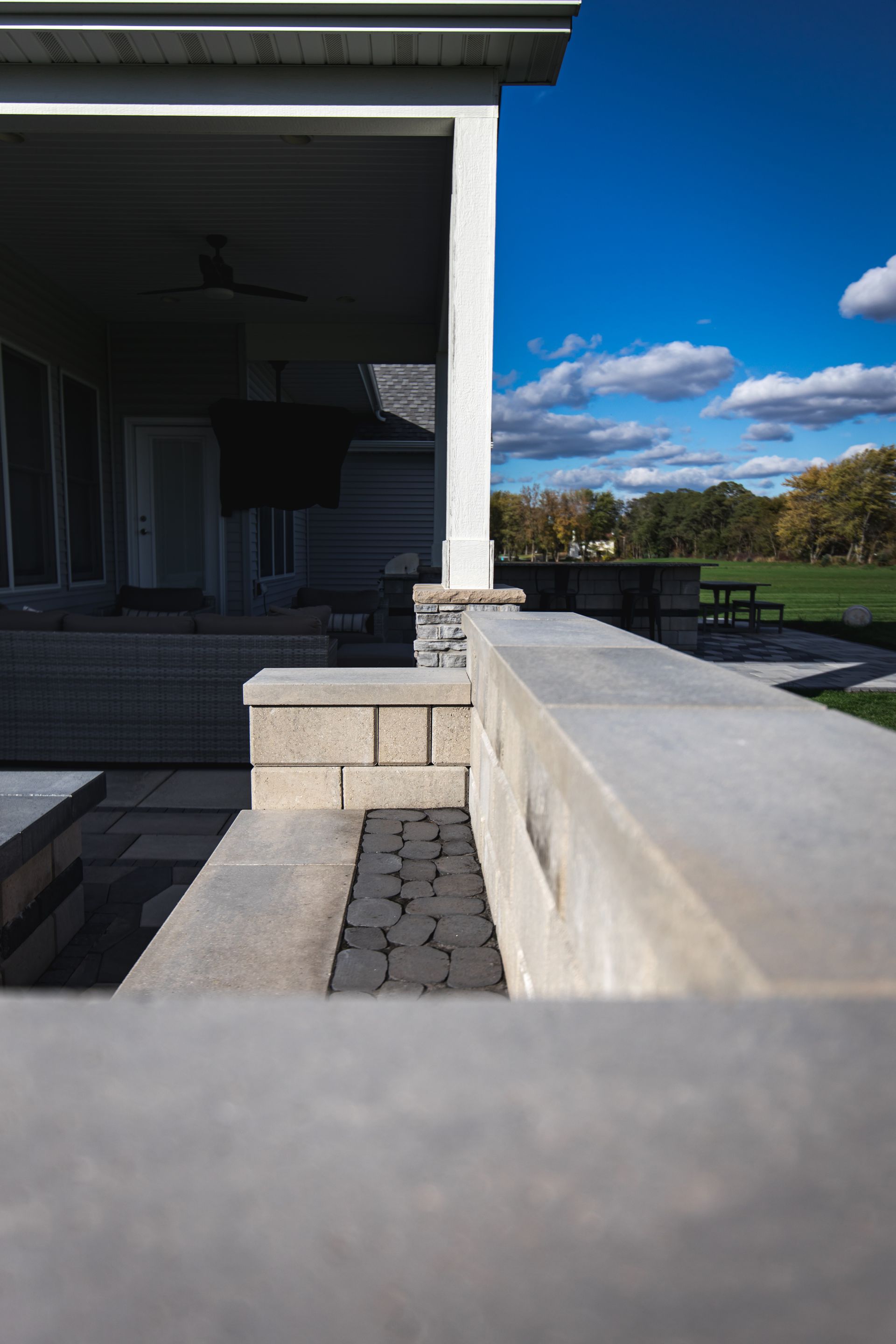 A modern patio with a concrete wall, a covered porch, and a view of a blue sky and park.