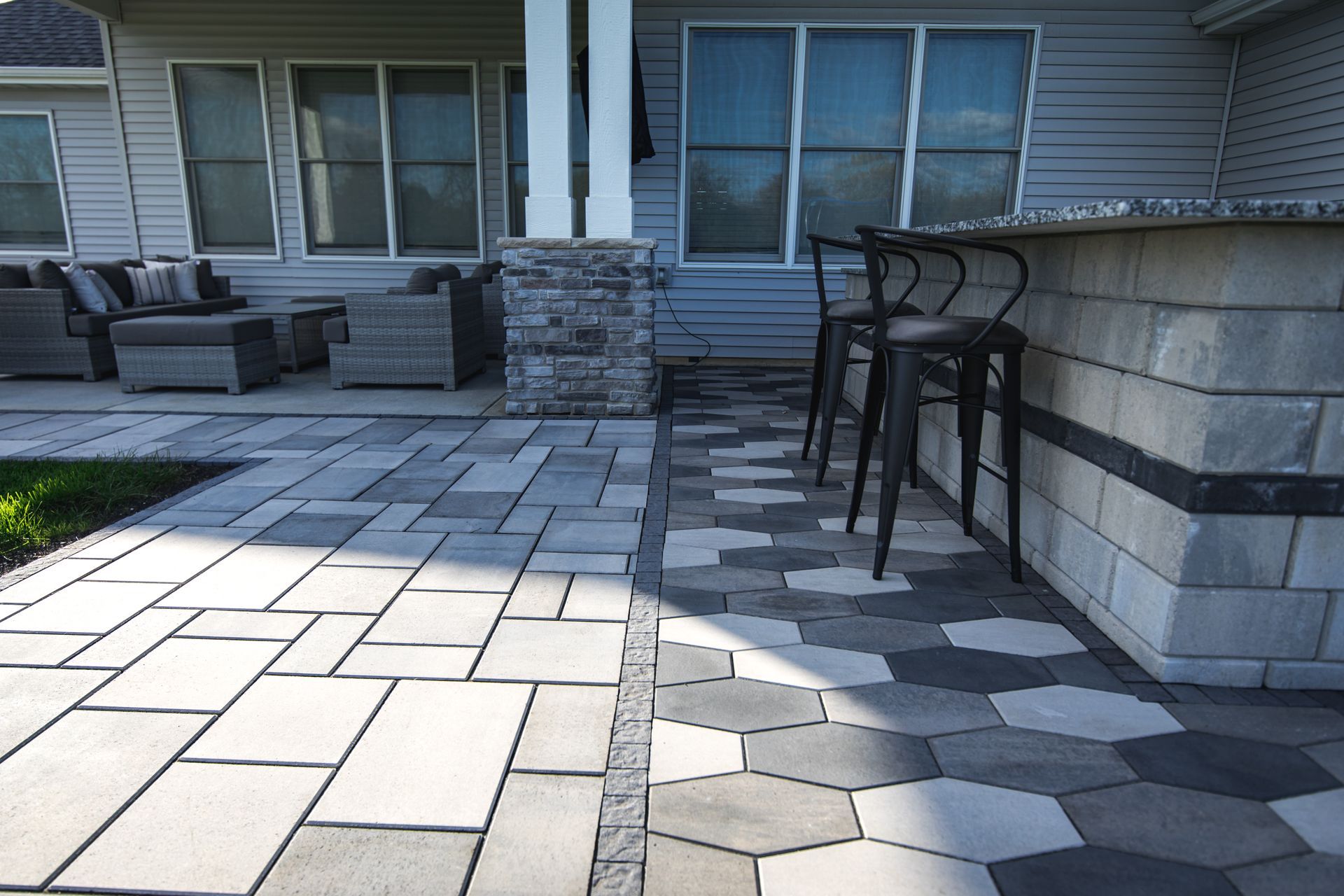 Patio with stone pavers and bar seating. Gray and white stone patio with outdoor furniture and a bar.