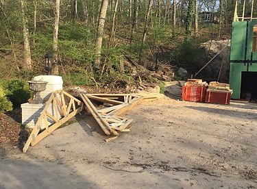 Construction site with wood trusses, bricks, and partially built structure. Trees in the background.