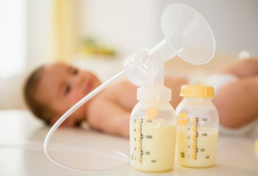Un neonato è sdraiato sul pavimento accanto a un tiralatte e a dei biberon di latte.