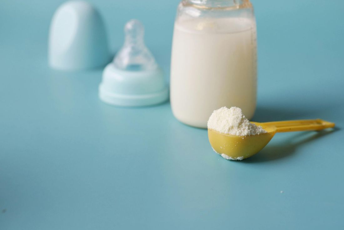 Una bottiglia di latte e un cucchiaio di latte artificiale su un tavolo blu.