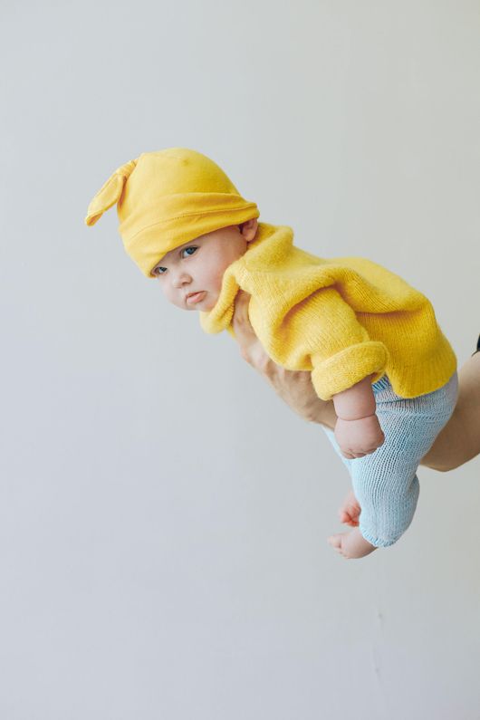Un bambino che indossa un cappello giallo e un maglione giallo è tenuto in braccio da una persona.