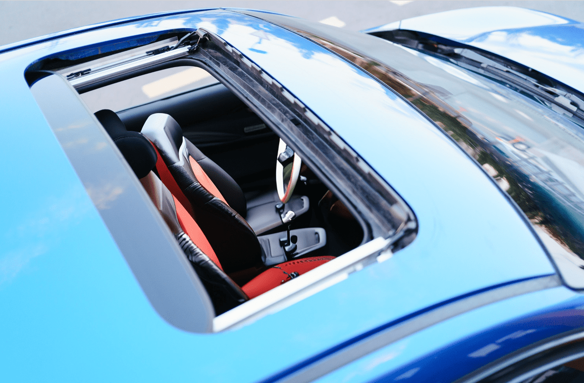 A blue car with the sunroof open and a red seat