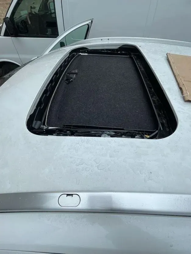 A silver car with a sunroof is parked next to a white van.