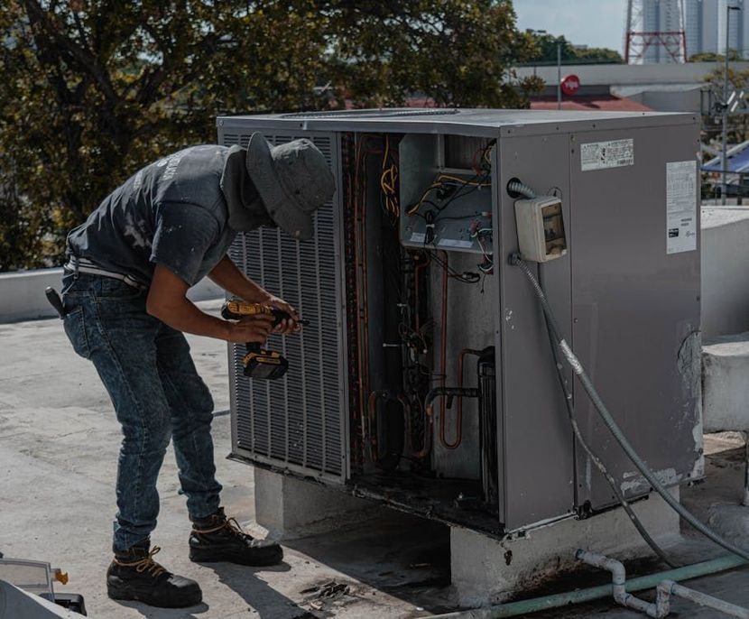 A man is working on an air conditioner on a roof.