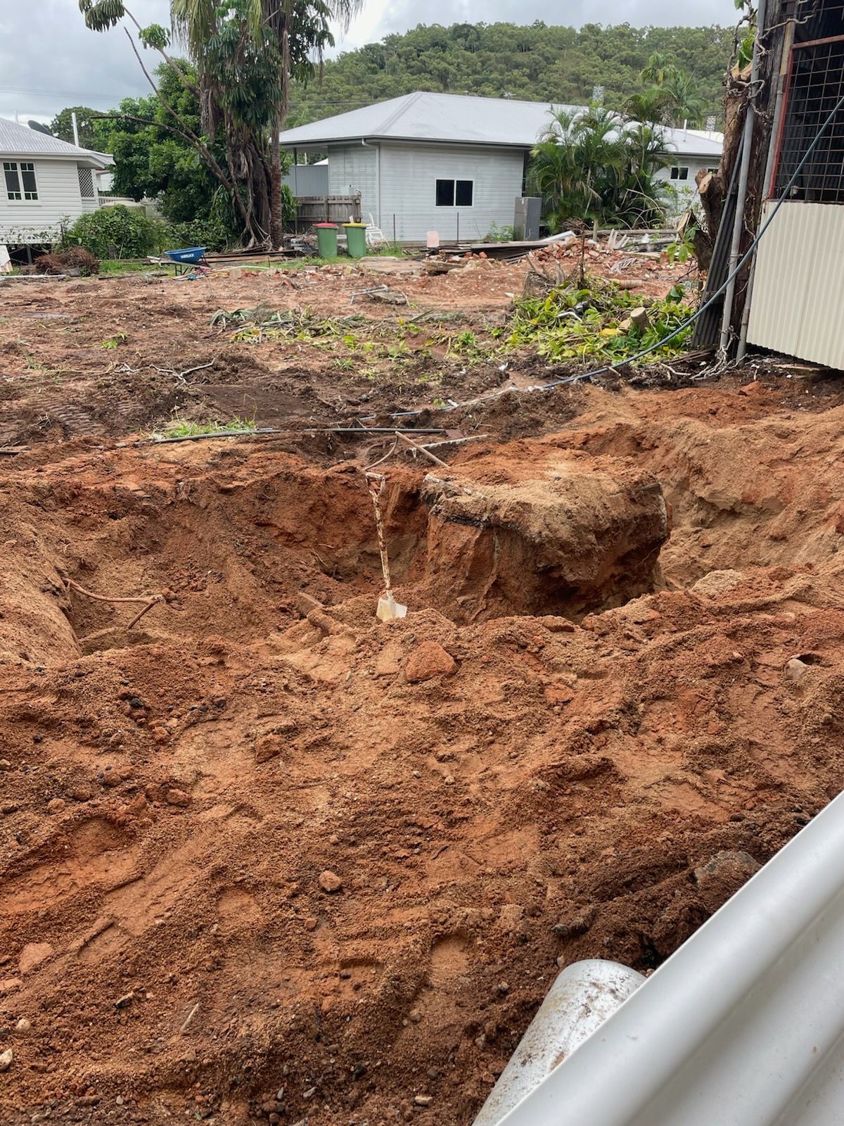 A large excavated pit in brown earth; a cleared lot with houses in the background.